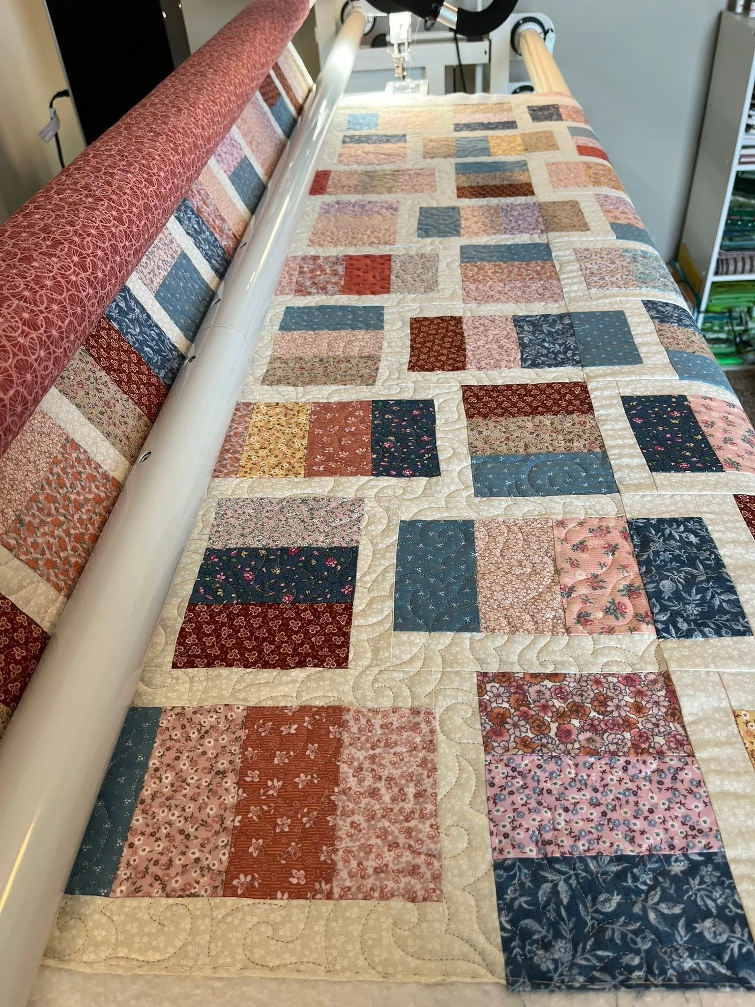 Close-up of a colorful patchwork quilt on a bed, with a fabric roll on the side.