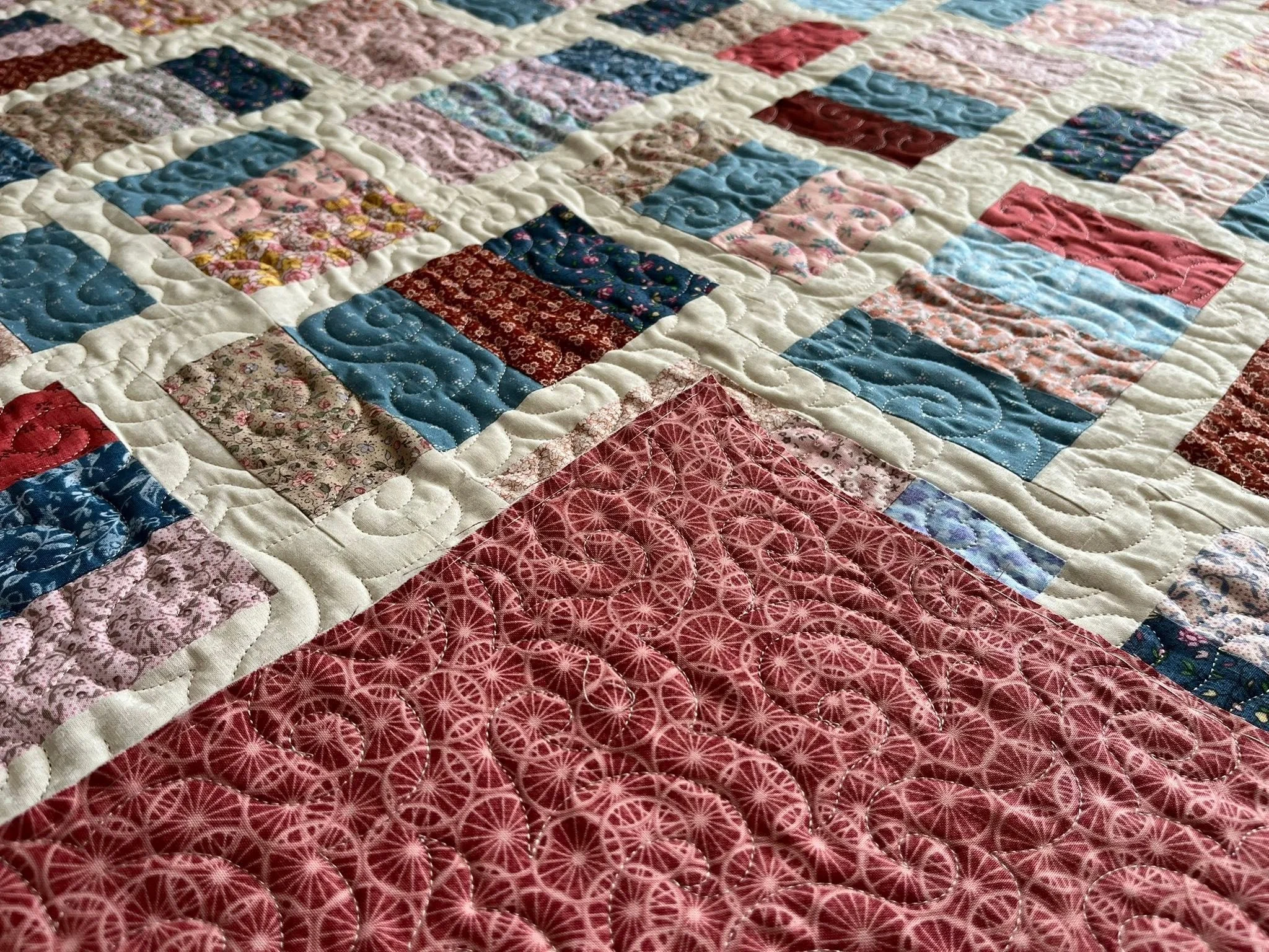 Close-up of a colorful quilt with various patterned fabric squares and white stitched borders.