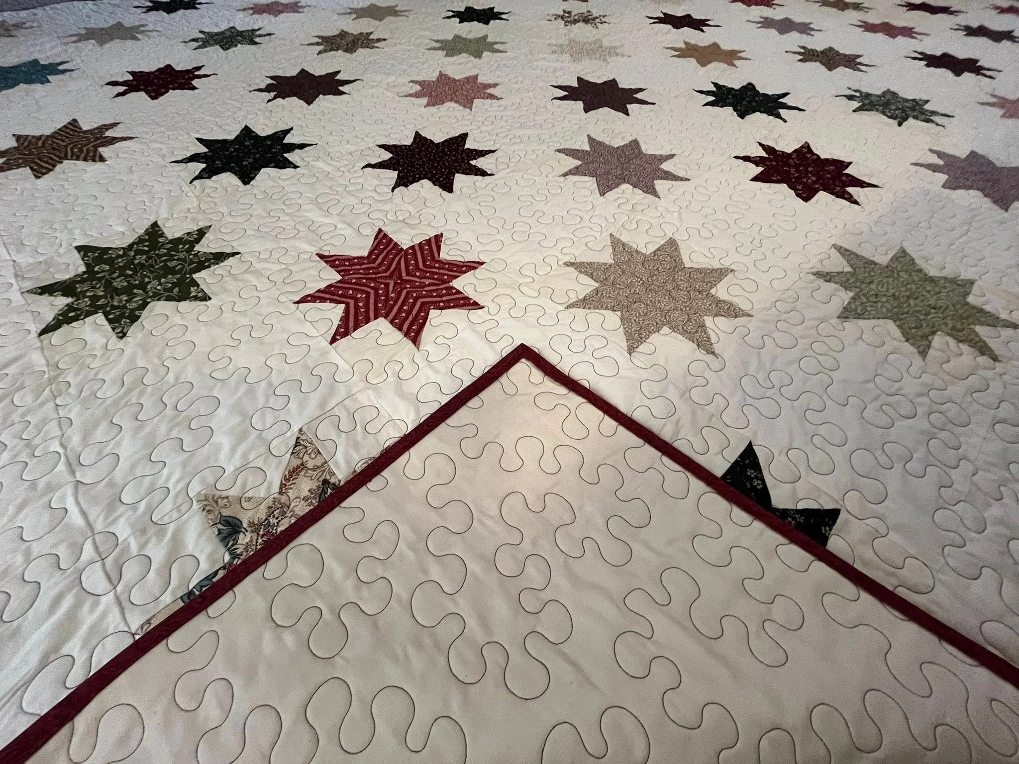 A partially completed quilt with a pattern of colorful star shapes on a white background, featuring a red border.