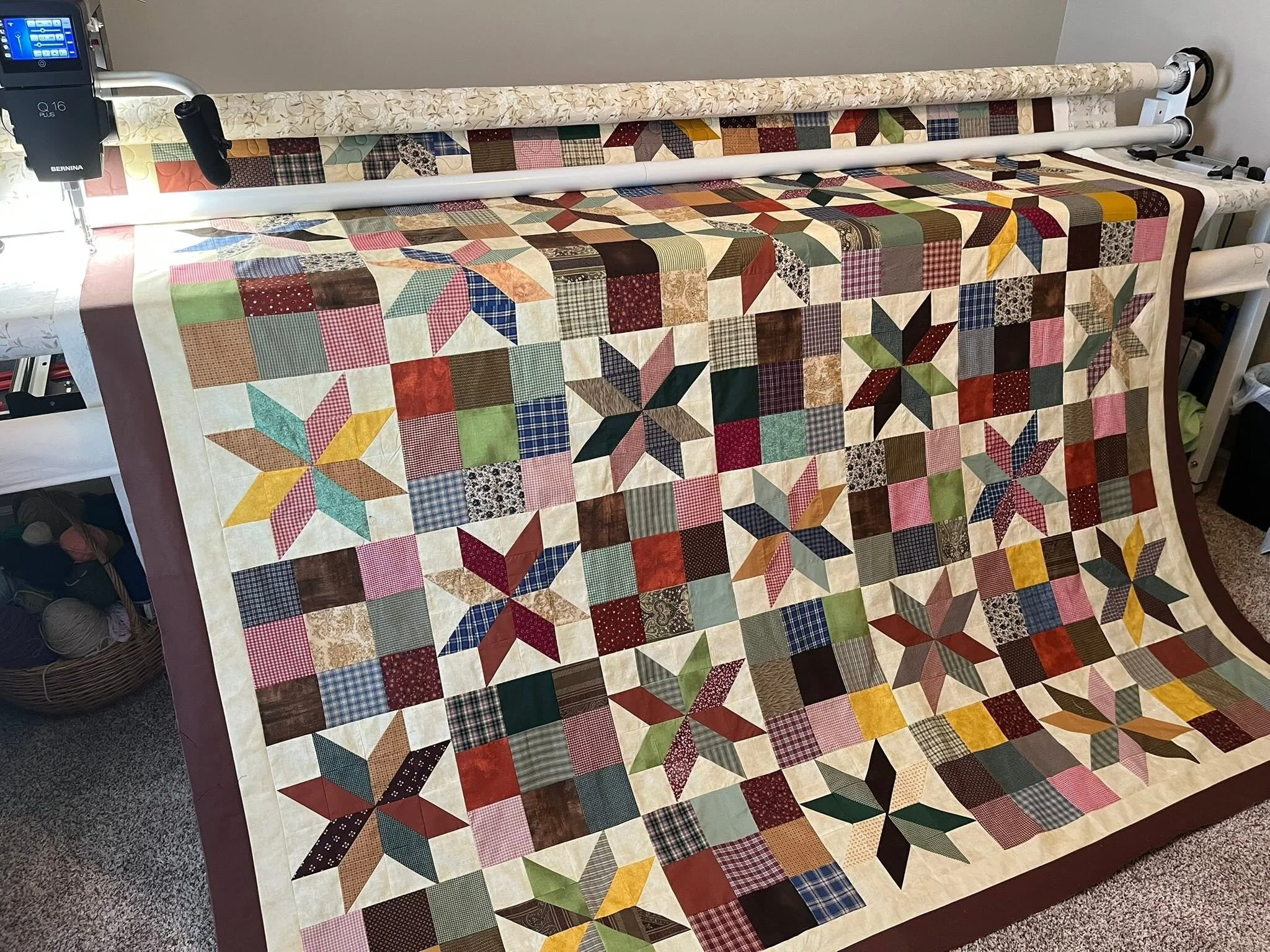 A colorful quilt with various patchwork patterns and pinwheels, draped over a quilting frame in a sewing room.