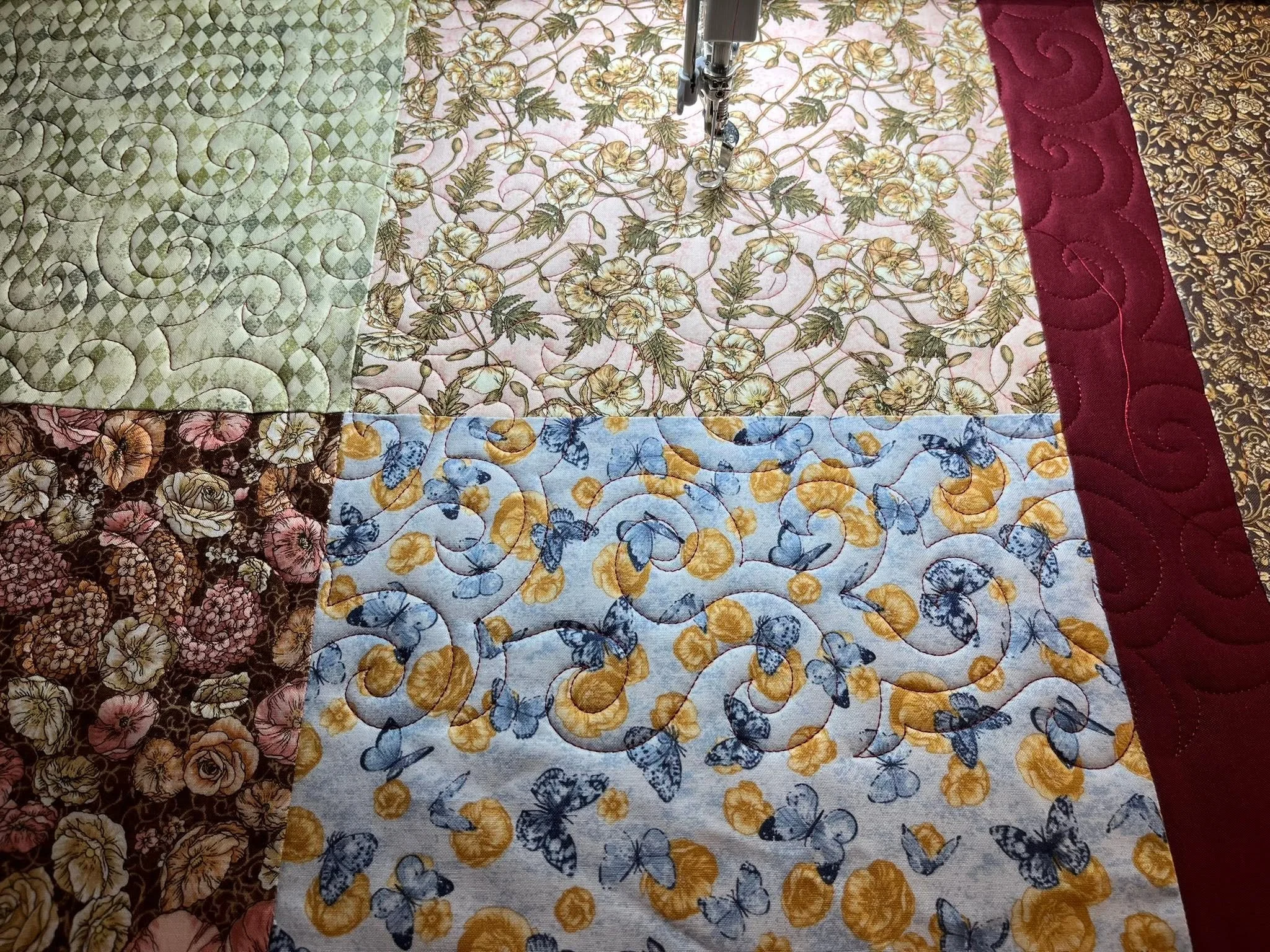 Various colorful quilt fabrics with floral and geometric patterns, stitched together, with a sewing machine needle in the center.