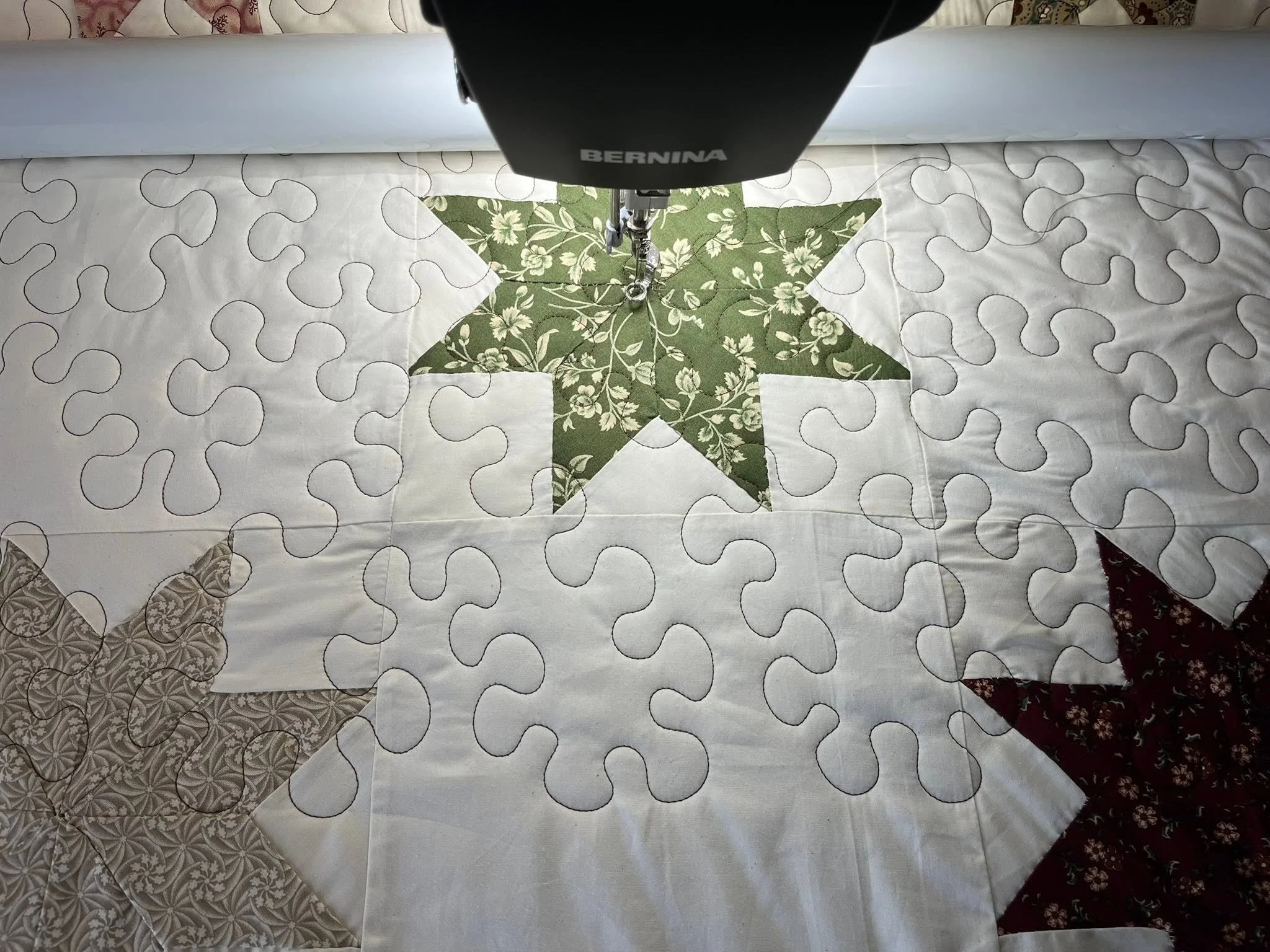 A sewing machine stitching a green and white floral fabric with a star shape in the middle, on quilted fabric.