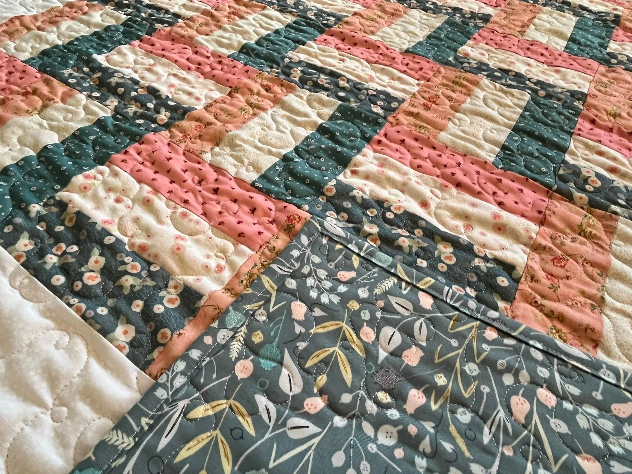 Close-up of a patchwork quilt with floral and patterned fabric in shades of pink, navy blue, and beige.