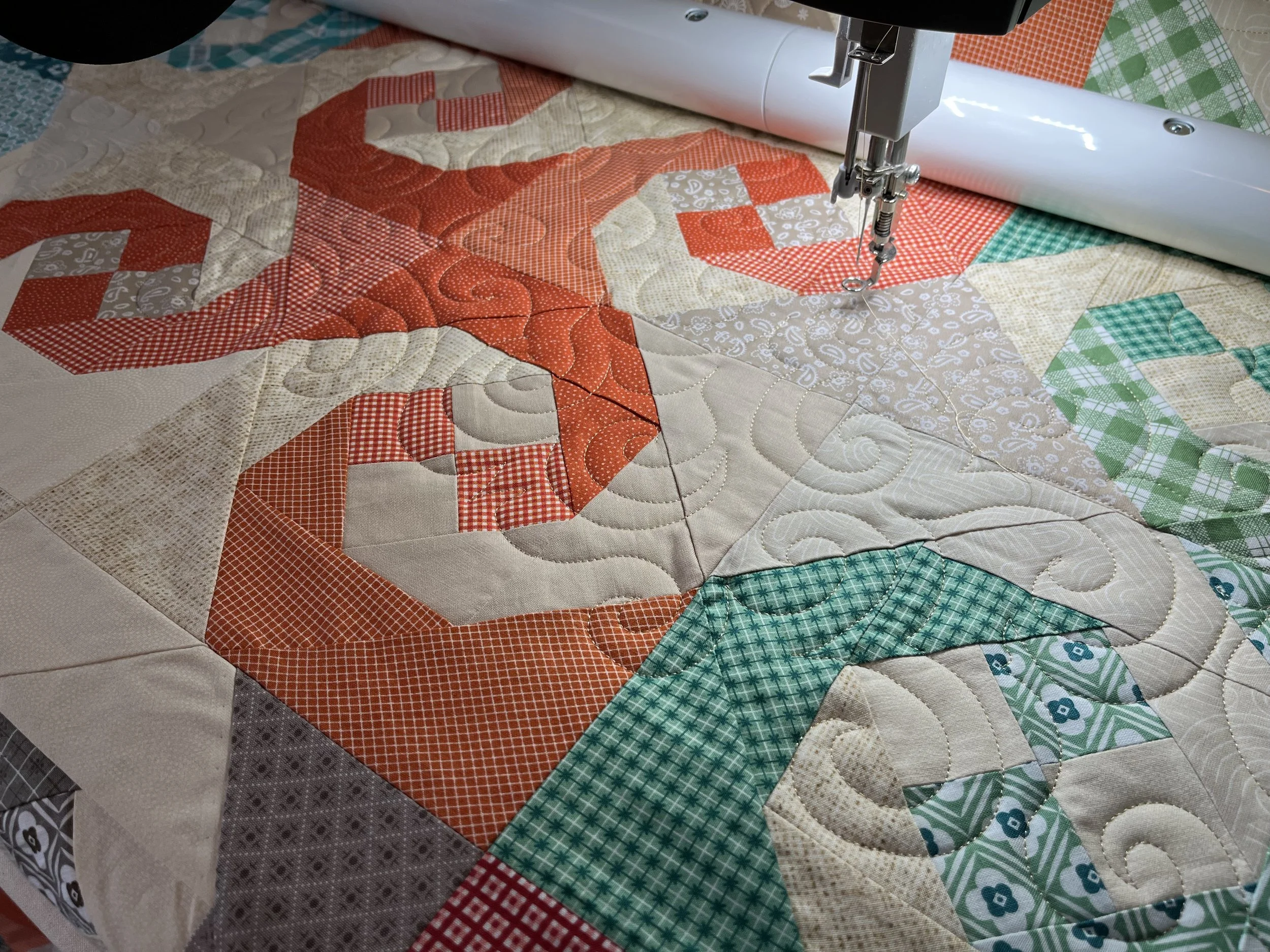 Close-up of a quilting machine stitching a patchwork quilt with red, beige, and green fabric pieces.
