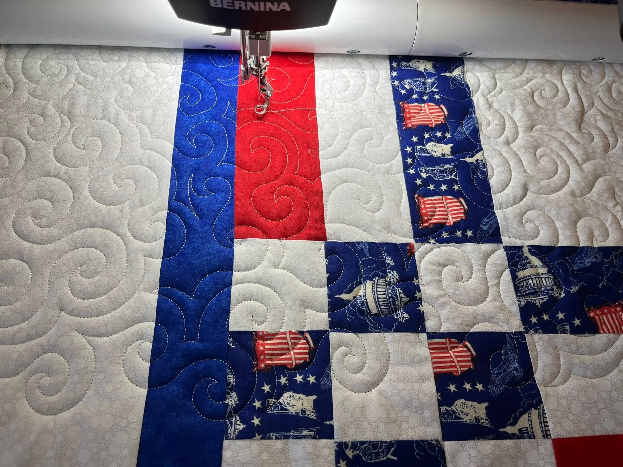 Close-up of a sewing machine stitching a patriotic quilt featuring red, white, and blue fabric with stars and stripes.
