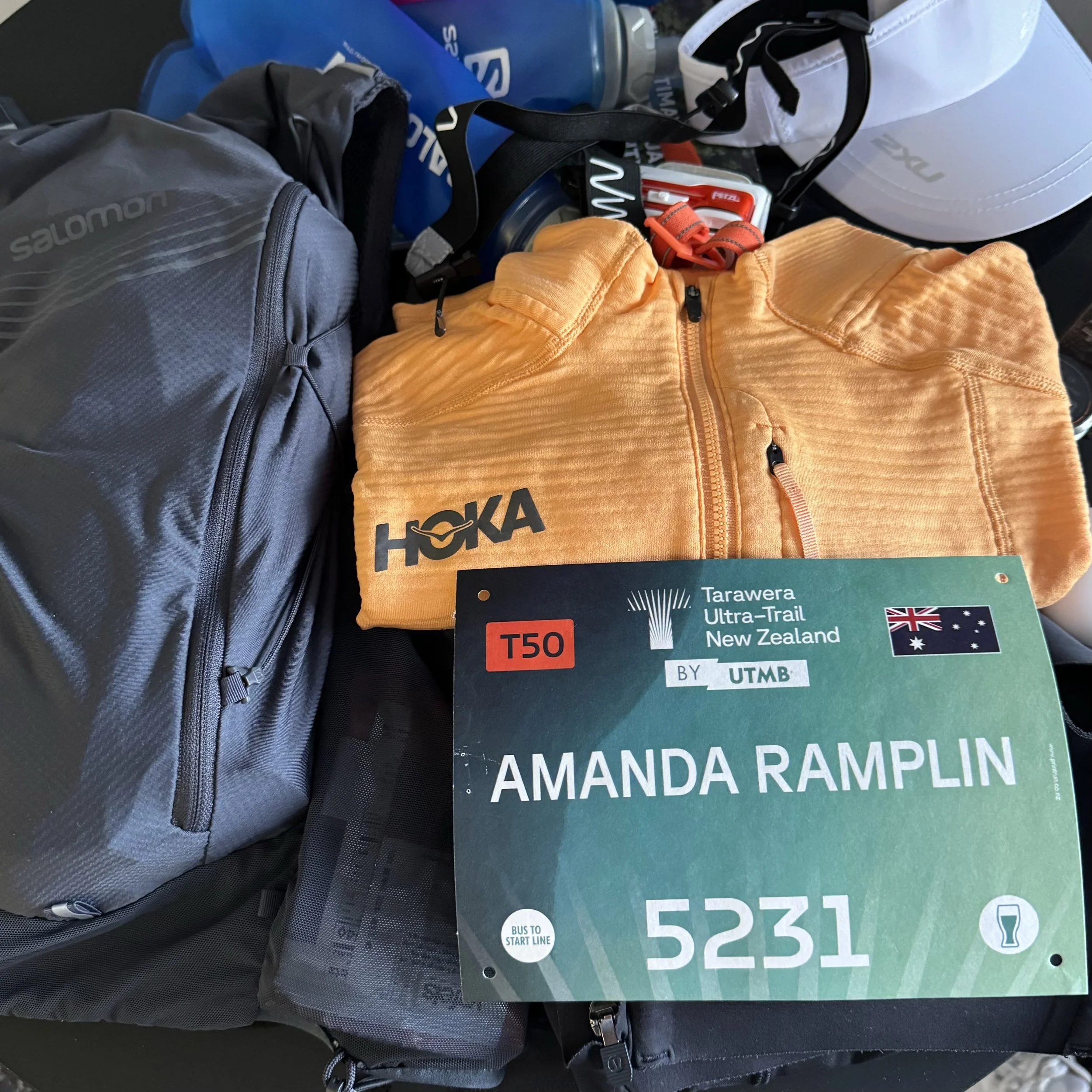 A hydration vest, folded jacket, head torch and race bib laid out