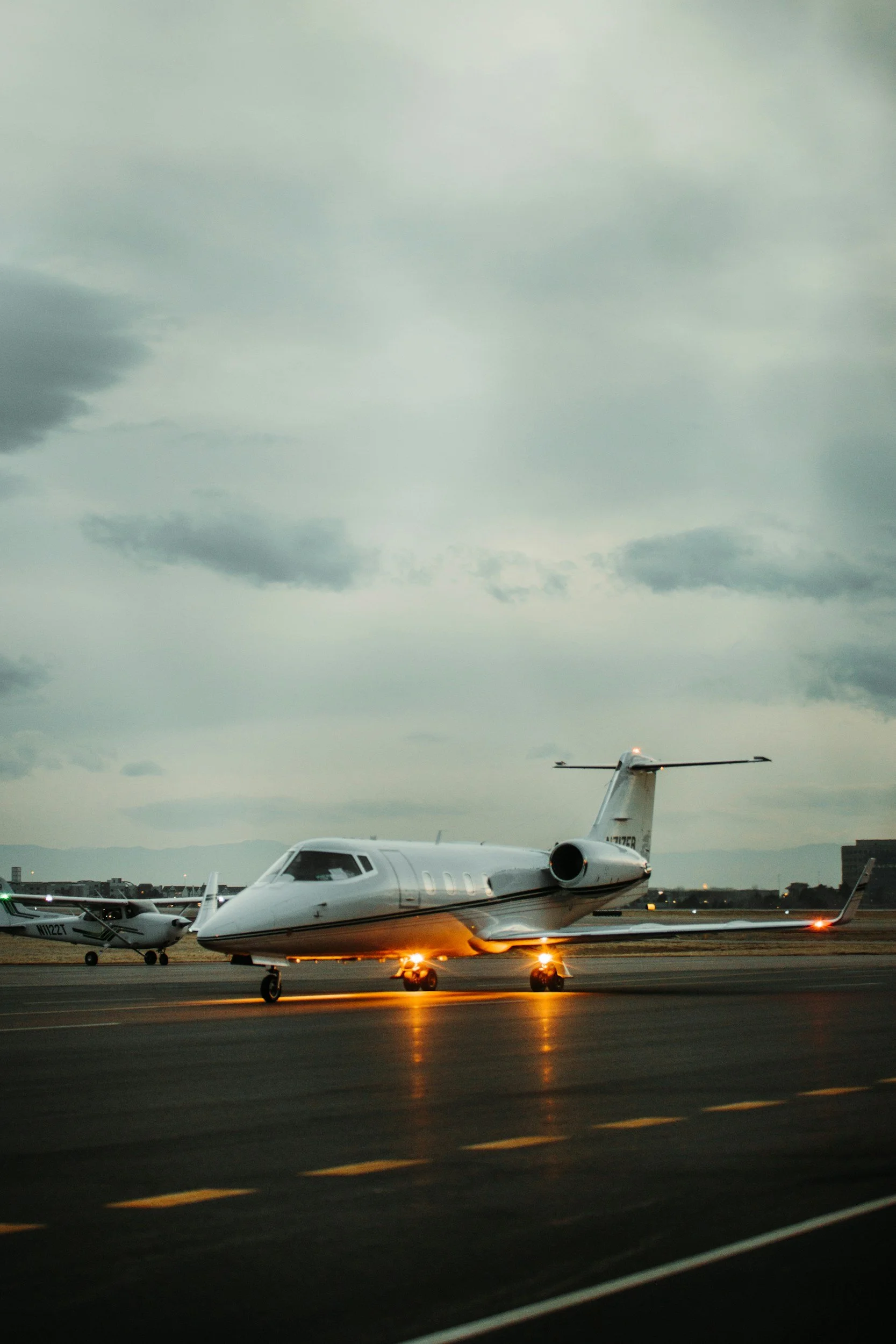 A private jet parked on an airport tarmac during dusk with cloudy skies overhead.