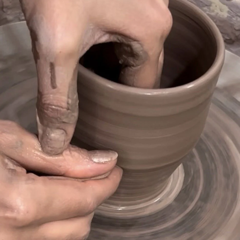 Close-up of a person's hands shaping a clay pot on a pottery wheel.