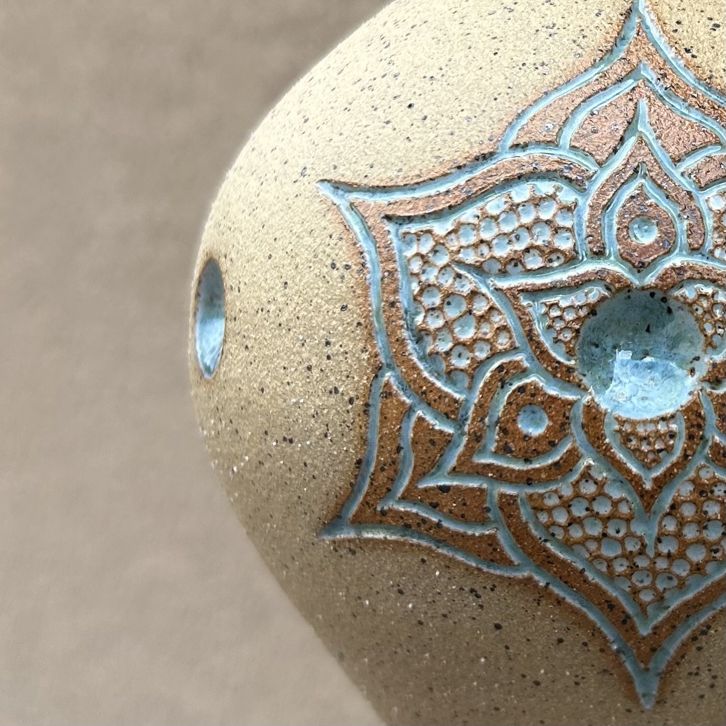 Close-up of a decorative ceramic object with carved blue designs on a textured beige surface.