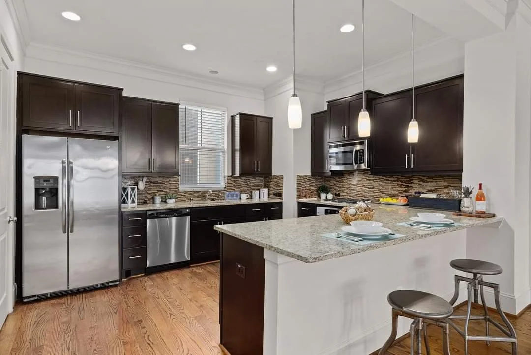 Modern kitchen with dark wood cabinets, stainless steel appliances, granite countertops, and a small breakfast bar with two stools. Kitchen appliance installation.