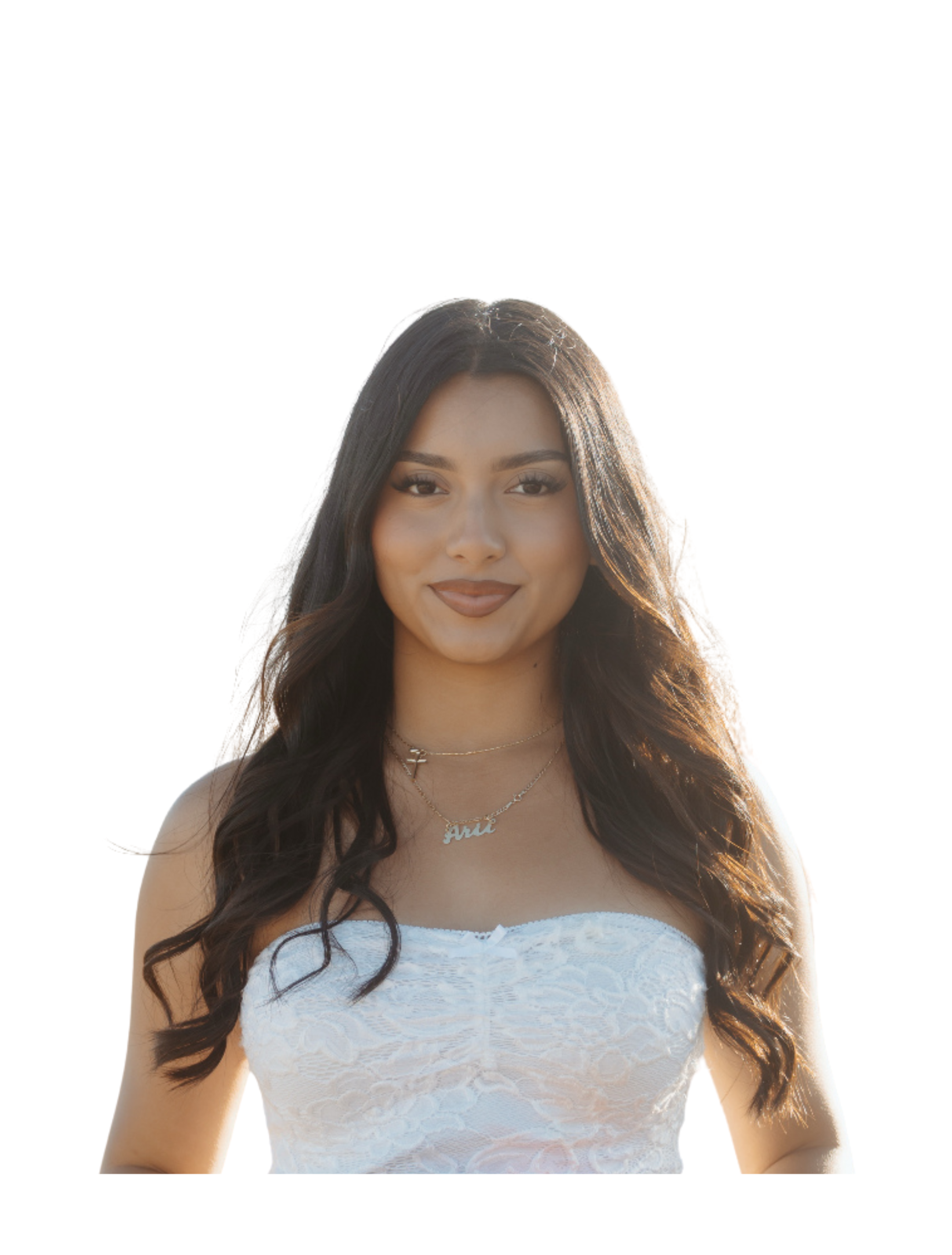 Close-up of a young woman with long dark wavy hair, wearing a white lace strapless top and layered necklaces, smiling softly against a bright white background.