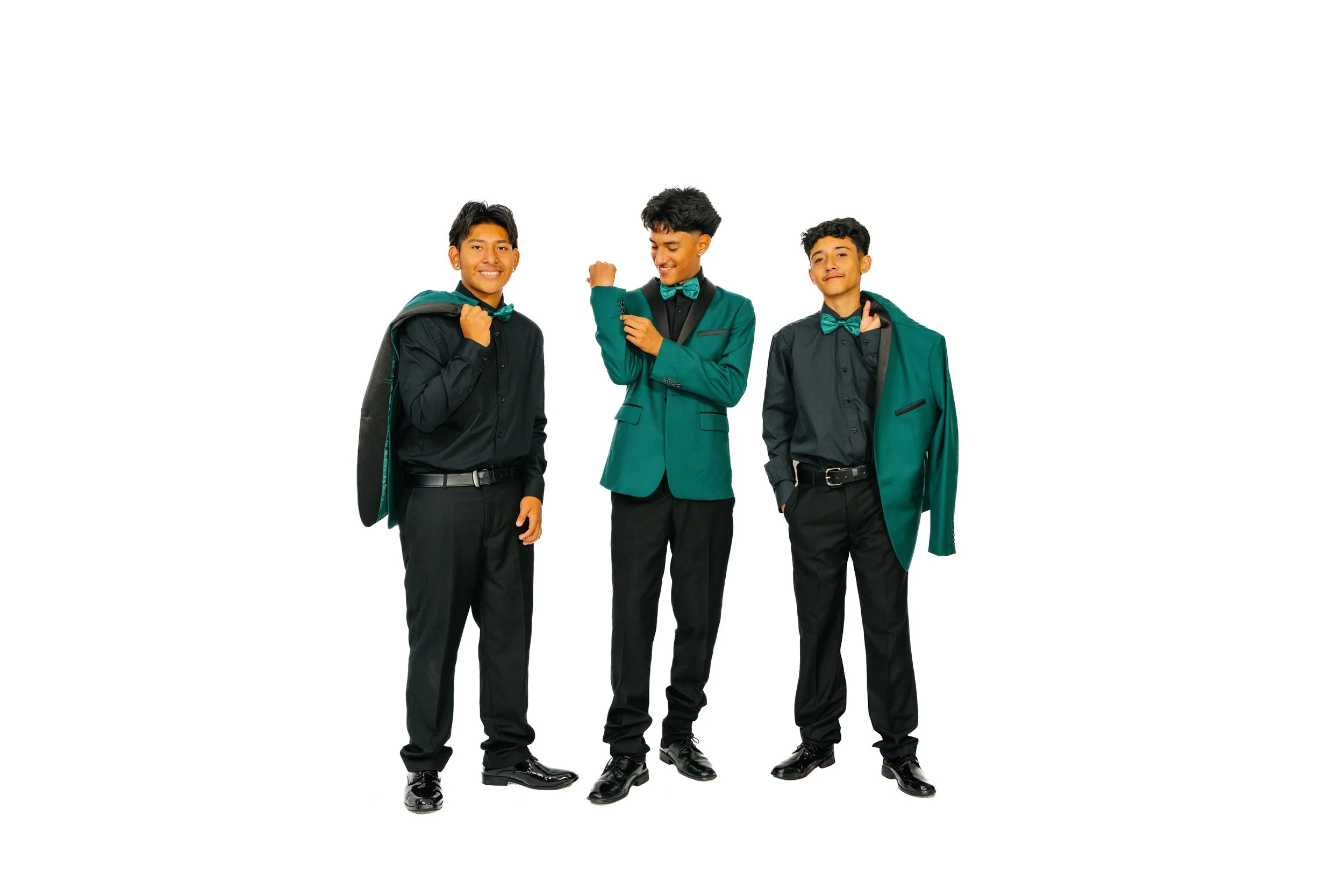 Three young men dressed in formal black and green suits, black dress shoes, and green bow ties, standing against a white background. They are smiling and showing confident poses, with two carrying suits or jackets over their shoulders.