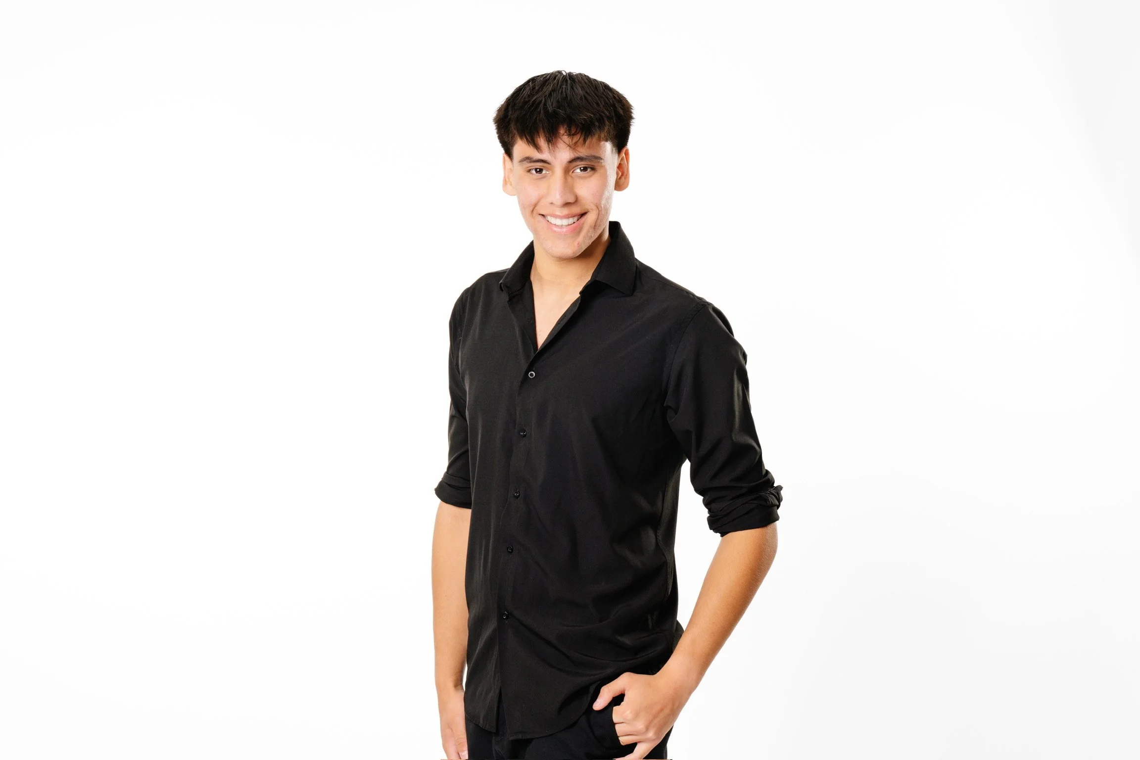 A young man with dark hair, smiling, wearing a black shirt with the sleeves rolled up, standing against a plain white background.