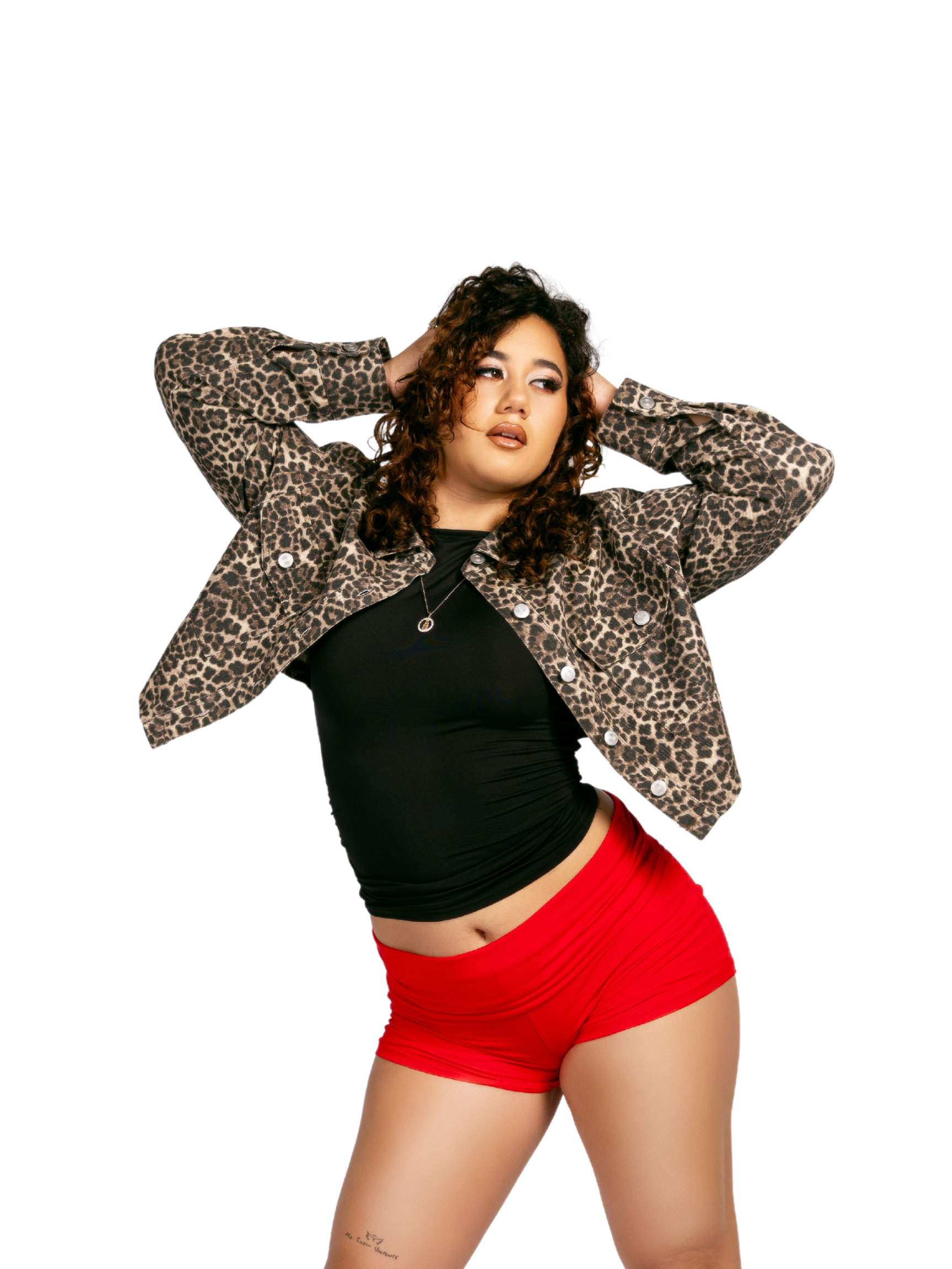 A woman with curly hair wearing a leopard print jacket, black top, and red shorts, posing against a white background.