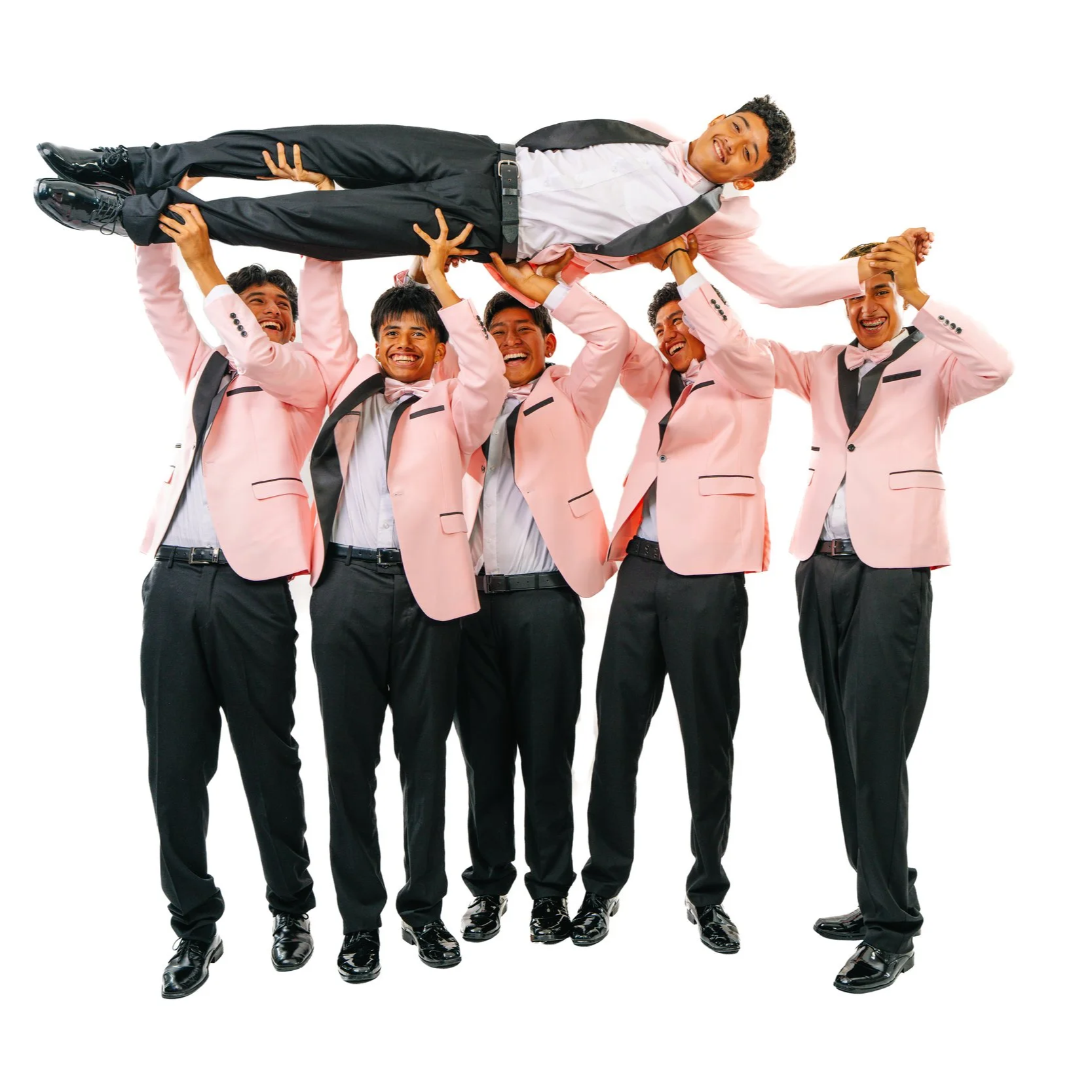 Group of five men in pink suits and black pants, lifting a man in a pink suit and black pants horizontally in the air, all smiling and laughing, against a white background.