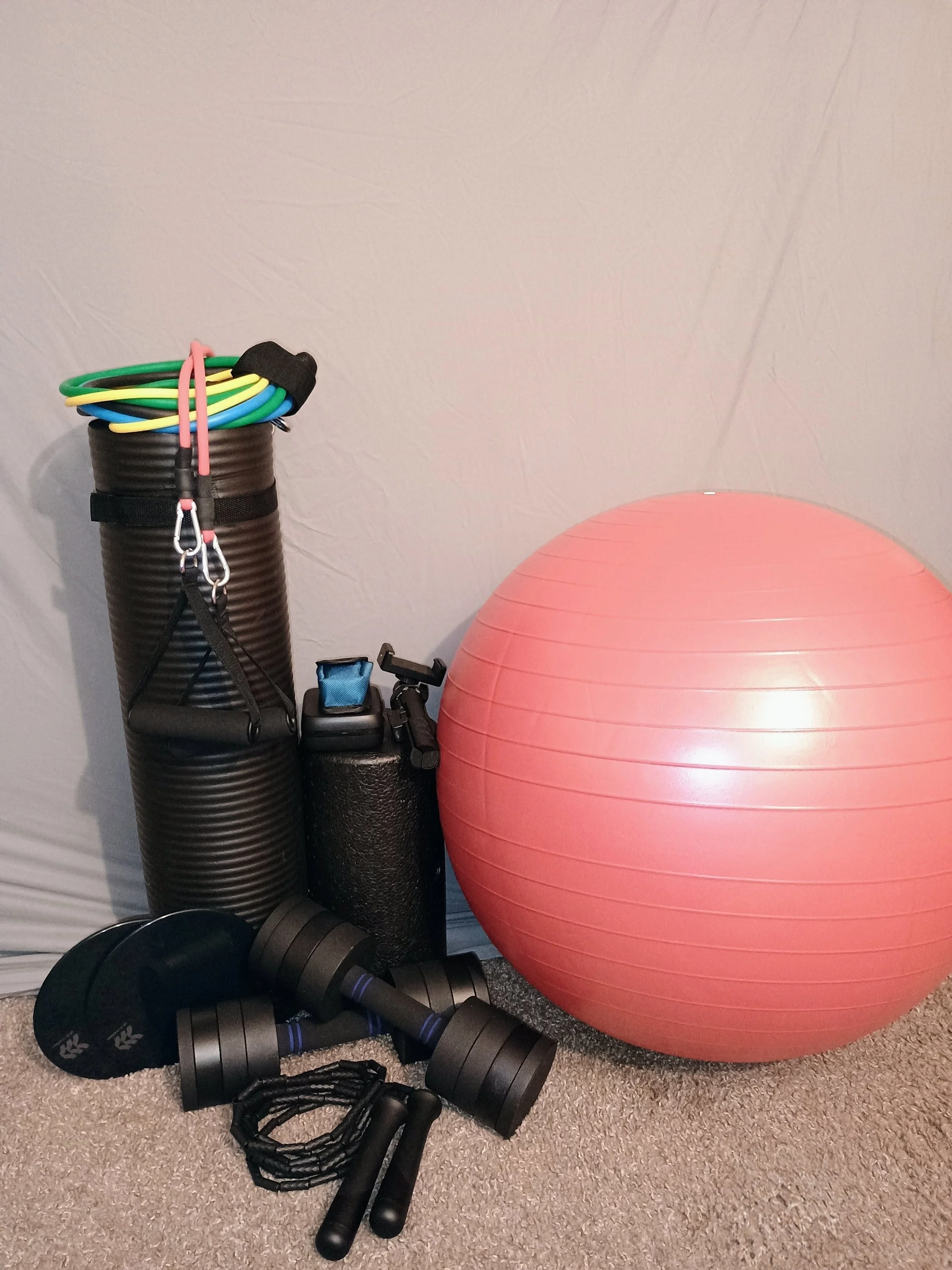 Assorted workout equipment including resistance bands, dumbbells, a stability ball, black foam rollers, and a jump rope