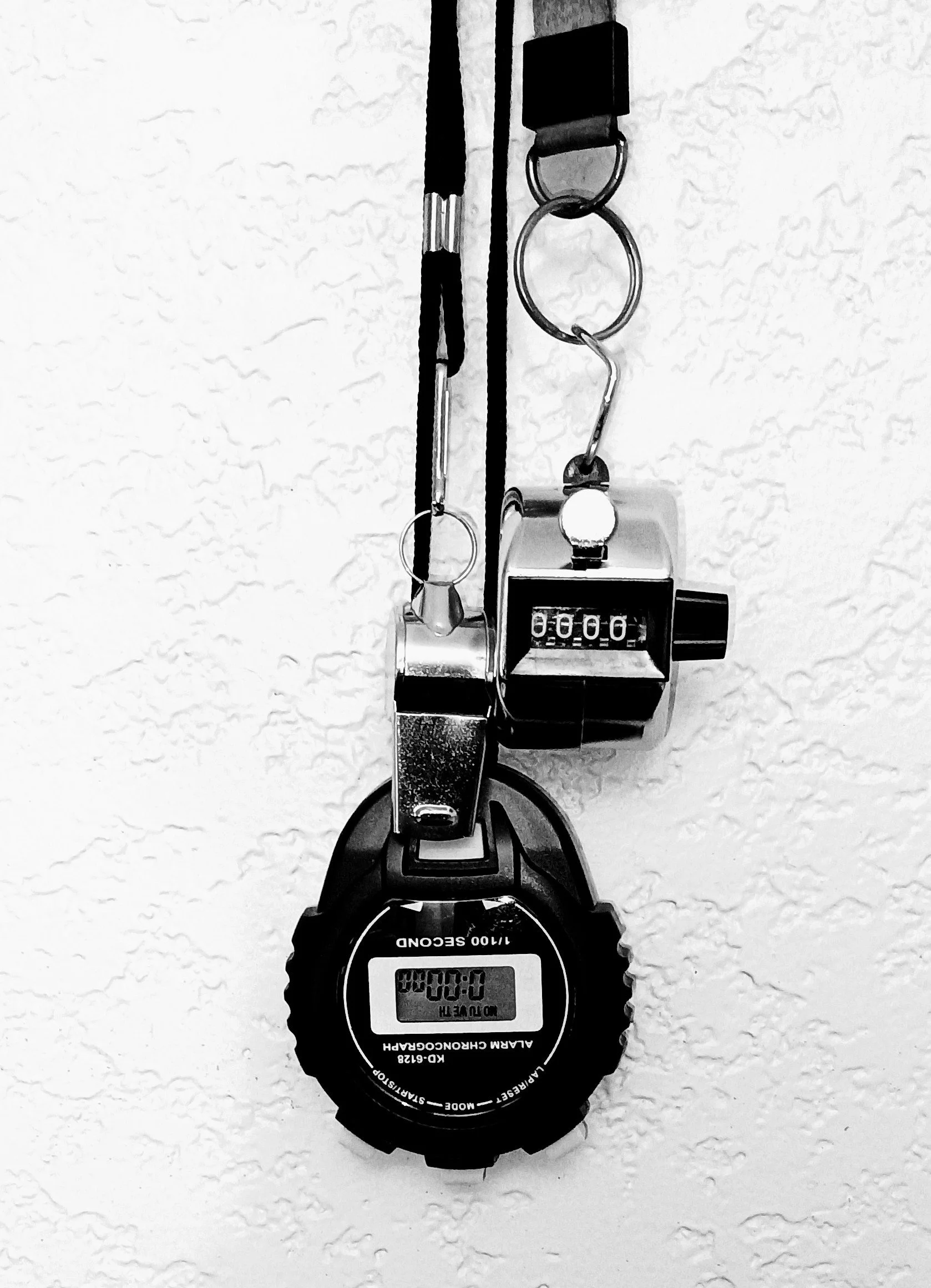 A digital stopwatch showing 0:00:00, attached to a limbo stick with a string, with a stopwatch placed on a textured white surface.