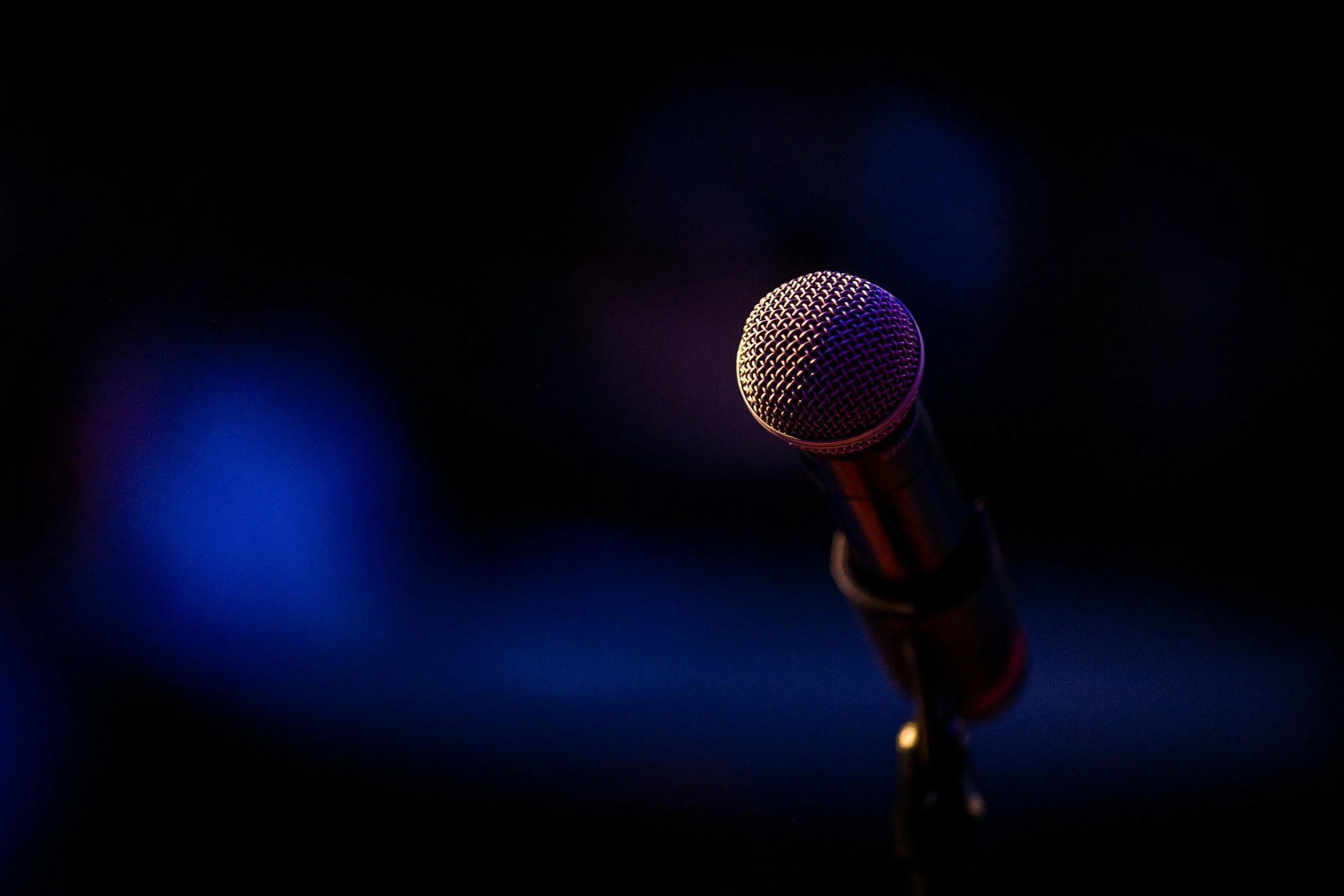 Close-up of a microphone in a dark setting with blurred colorful lights in the background.