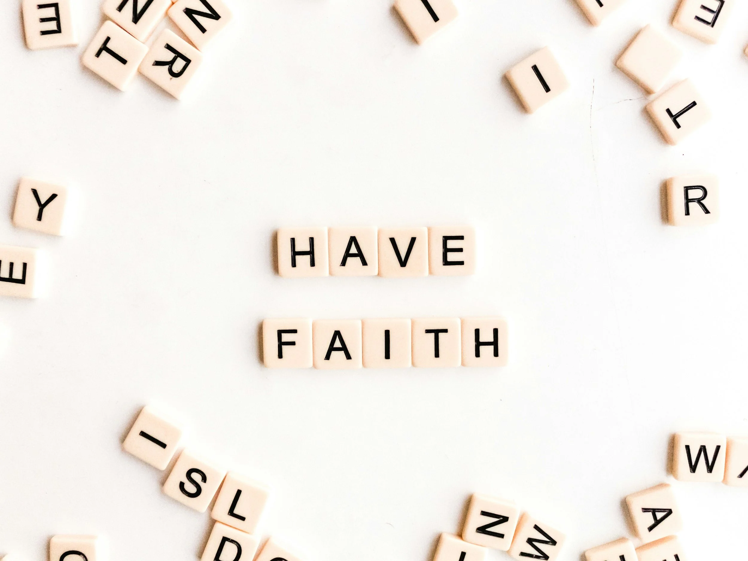 Letter tiles spelling out the words "HAVE FAITH" surrounded by scattered letter tiles on a white surface.