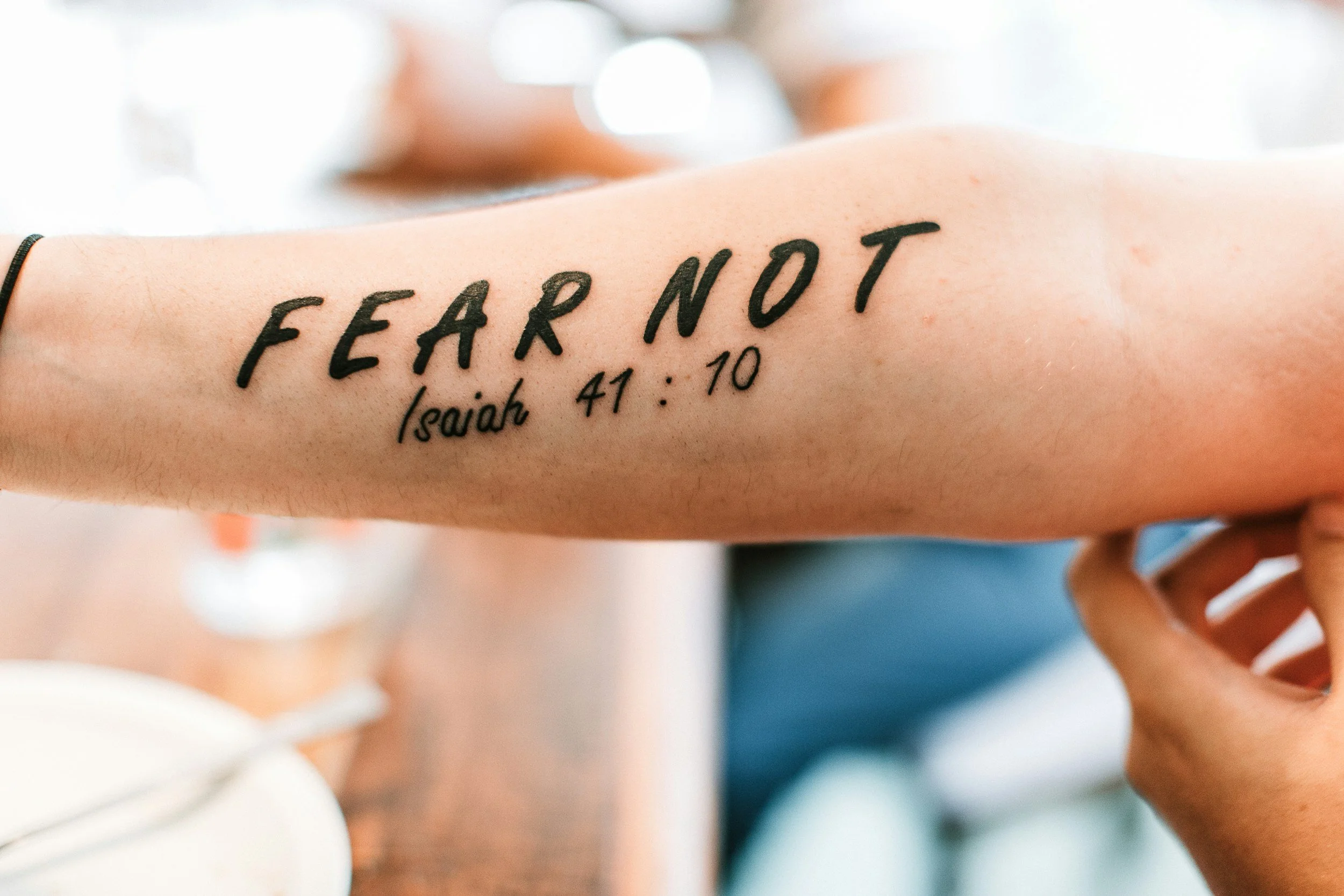 A person's forearm with a tattoo that reads "FEAR NOT" and a Bible verse reference "Isaiah 41:10" in black ink.