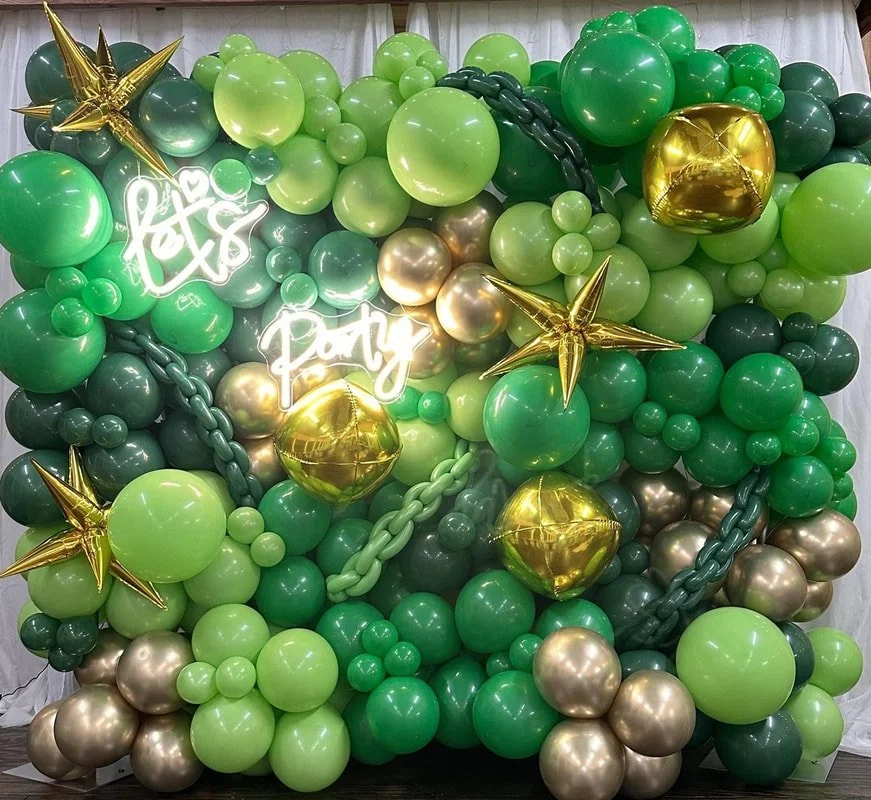 Green, gold, and dark green balloons arranged in a decorative backdrop with neon signs that say "Let’s Party" and gold star-shaped balloons.