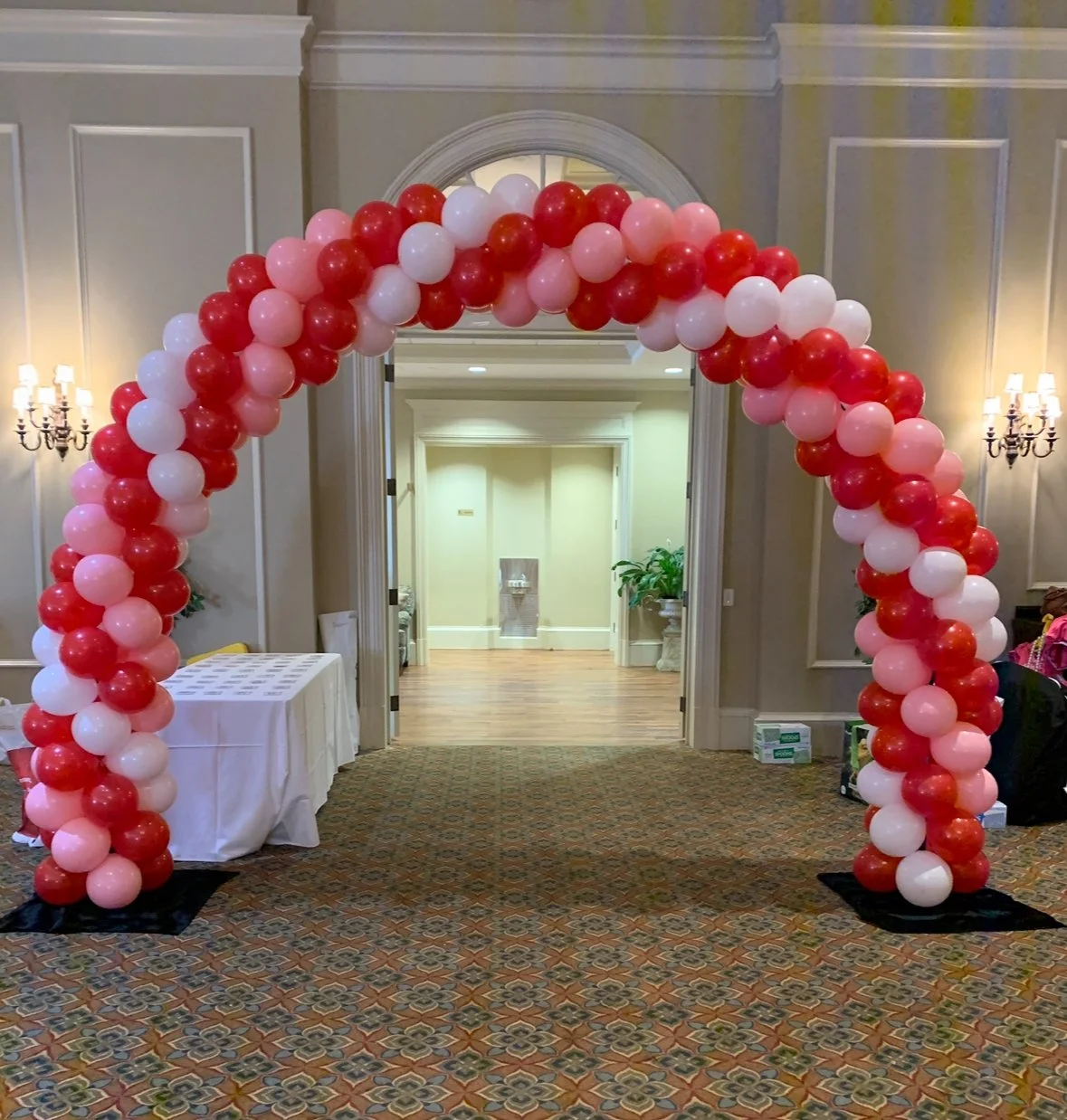 Red, pink, and white balloons arranged as an arch at an indoor event.
