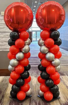 Two balloon columns topped with large red balloons, decorated with smaller black, red, and silver balloons arranged in a spiral pattern.
