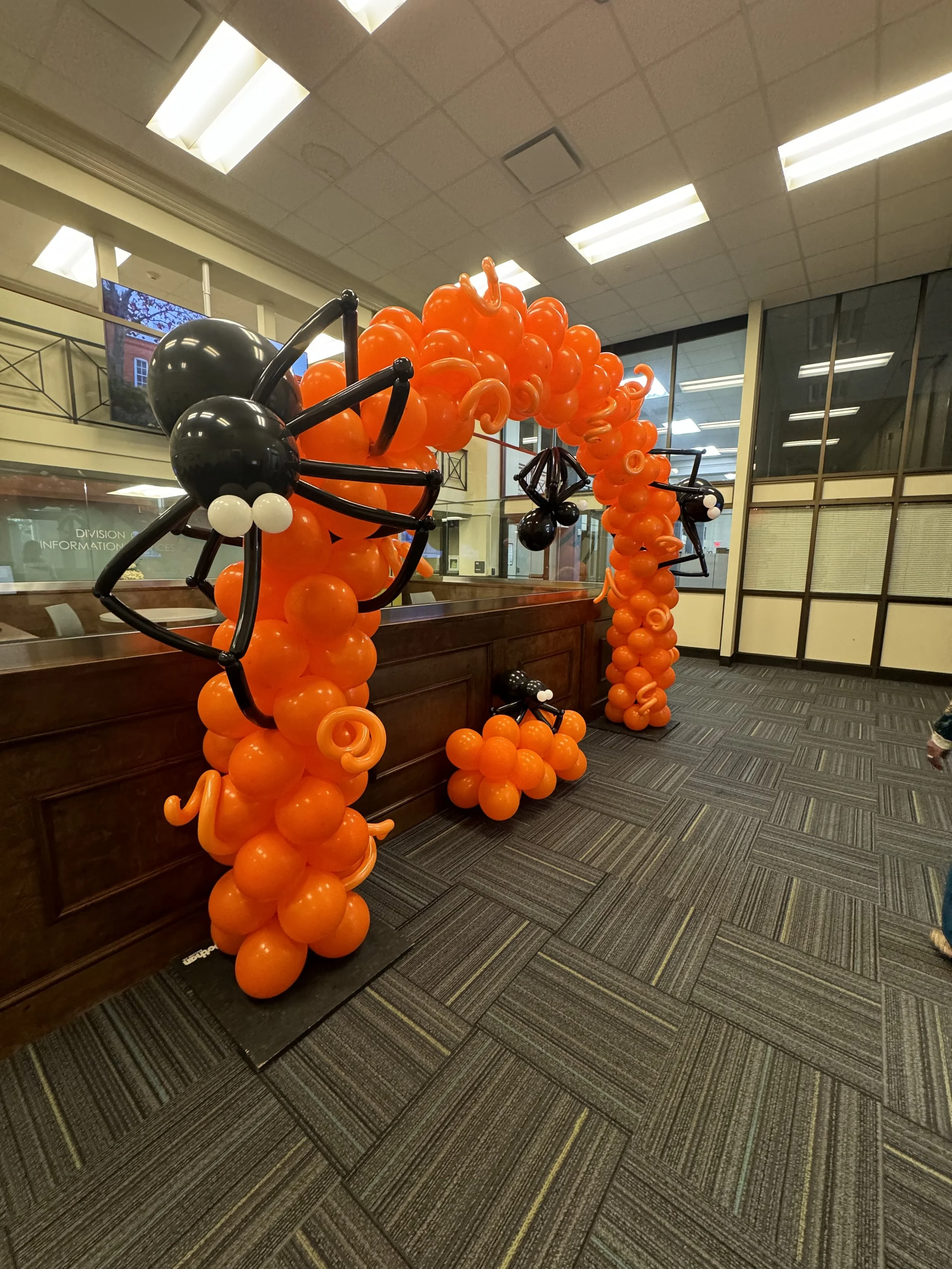 Decorative balloon arch and sculptures with black, white, and orange balloons inside a building.