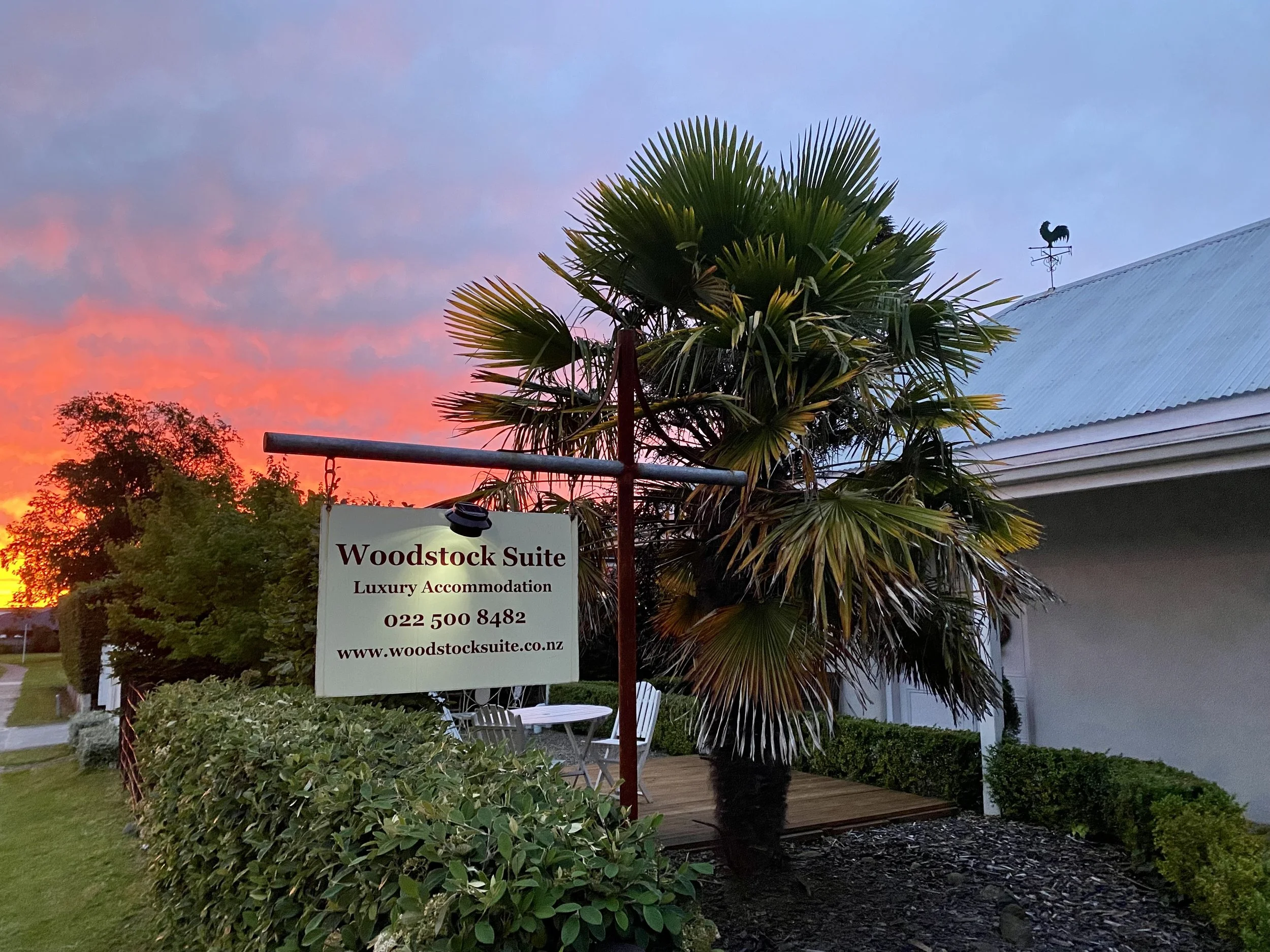 The front view of the Woodstock suite at sunset with palm trees in front of the building and the Woodstock Suite luxury accommodation sign.
