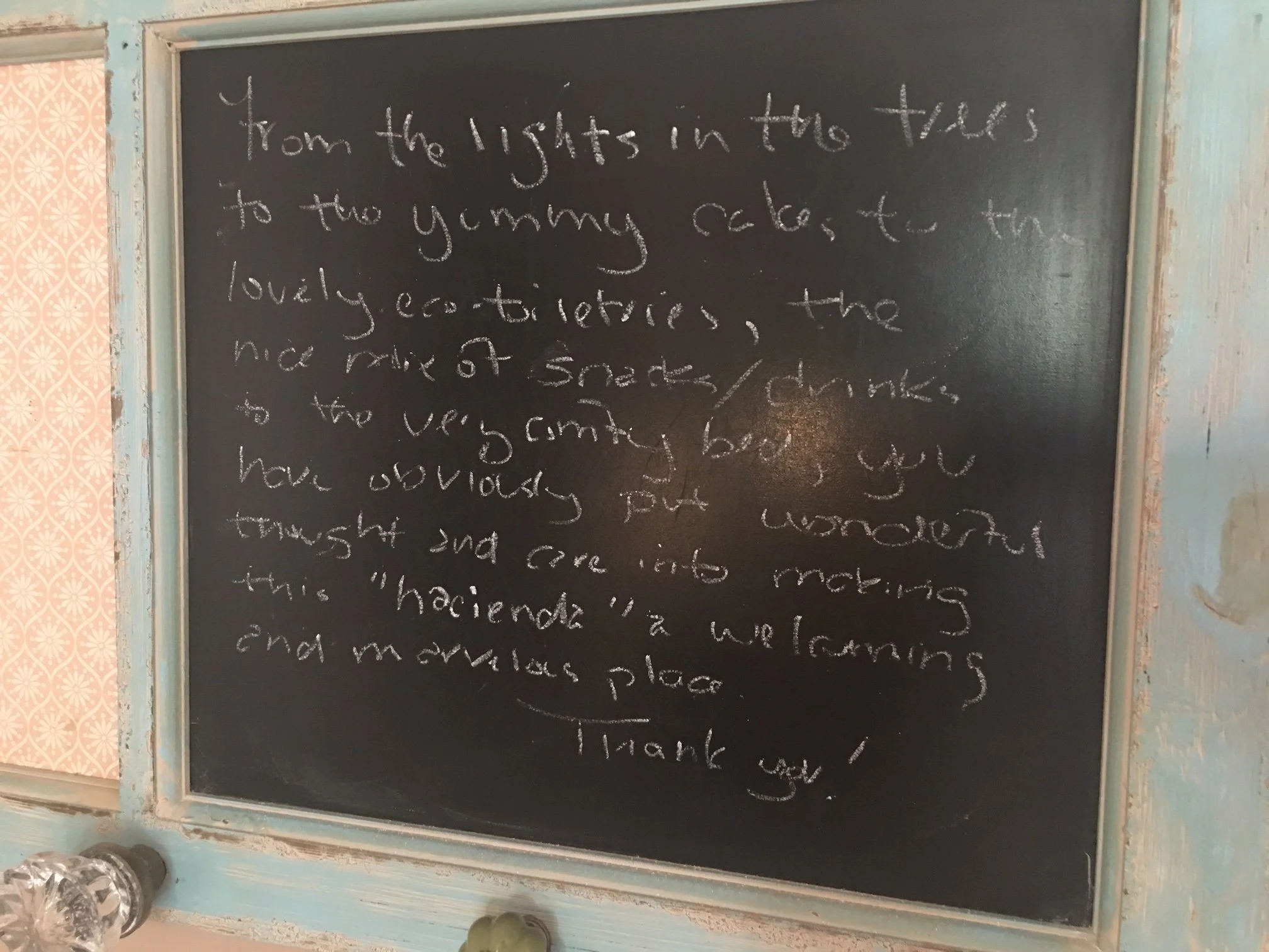A chalkboard with handwritten message about the lights in the travel trailer, decorated with a vintage frame and pink patterned wallpaper on the side.