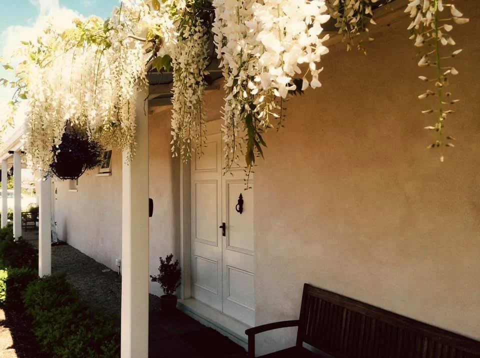 Front porch of the Woodstock Suite, decorated with hanging white flowers and greenery, featuring white double doors and a wooden bench.