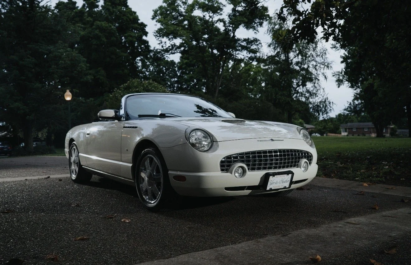A white convertible sports car parked on a street with trees and houses in the background during dusk.