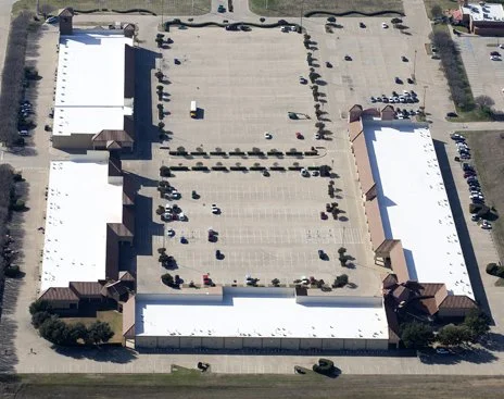 Aerial view of a large shopping mall parking lot with surrounding stores and parking spaces.
