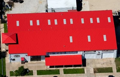 Aerial view of a long building with a red roof, parking lot, and surrounding sidewalks.