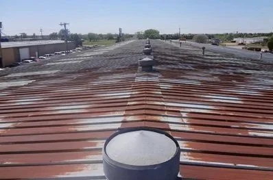View of a metal rooftop with multiple vents and rust-colored roof panels.