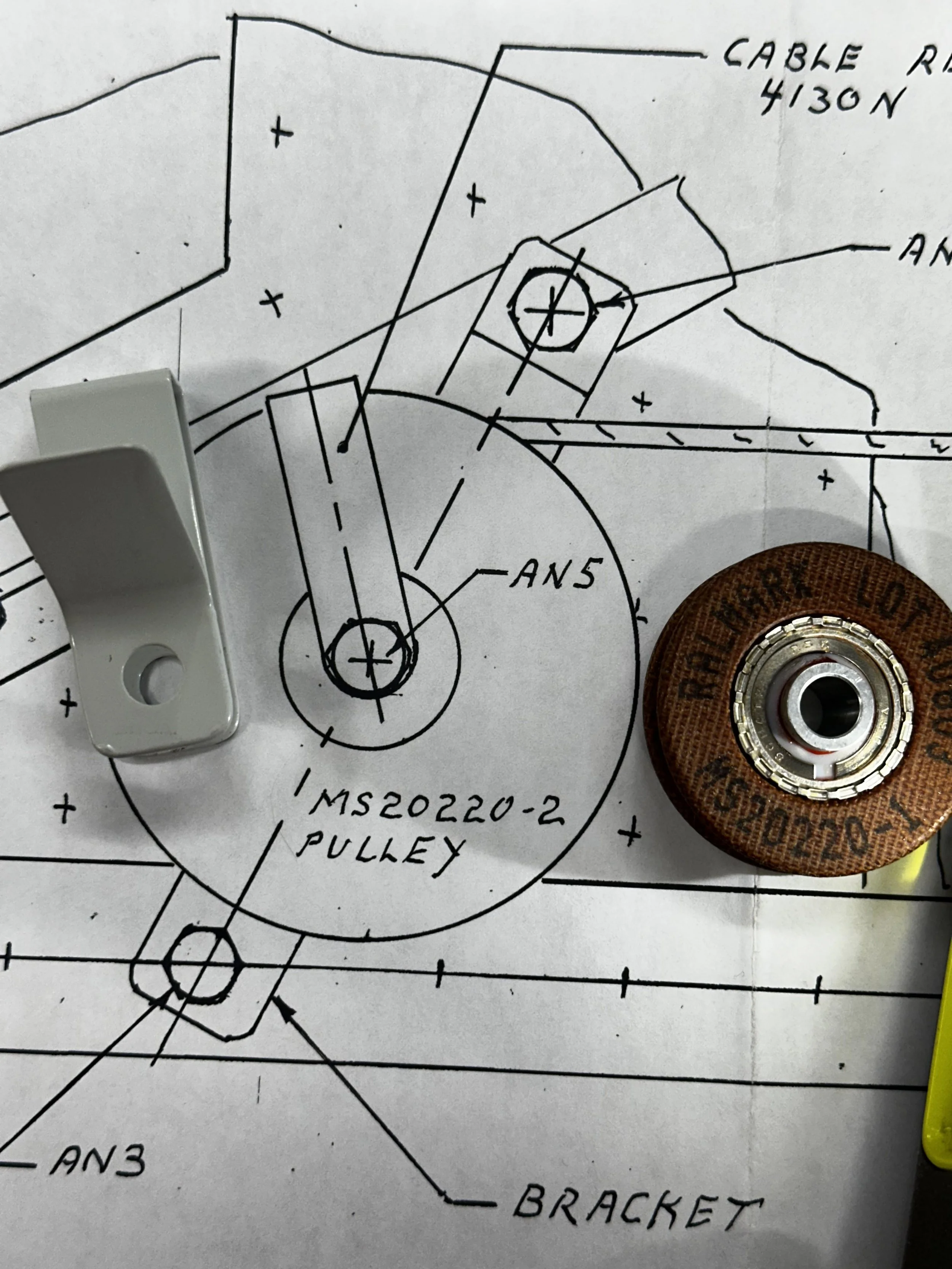 Hand-drawn technical illustration of a pulley assembly, labeled with parts such as cable, anchor, and bracket, on a detailed engineering drawing.