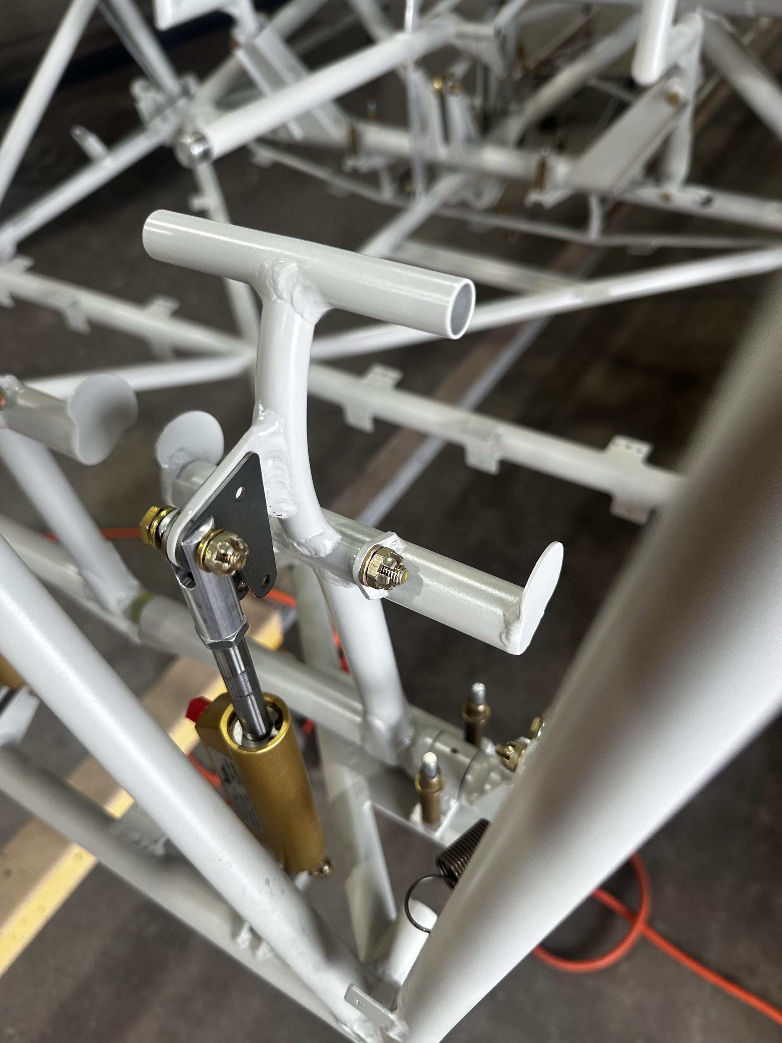 Close-up of a white metal frame with gold-colored suspension components, possibly part of a bicycle or motorcycle construction.
