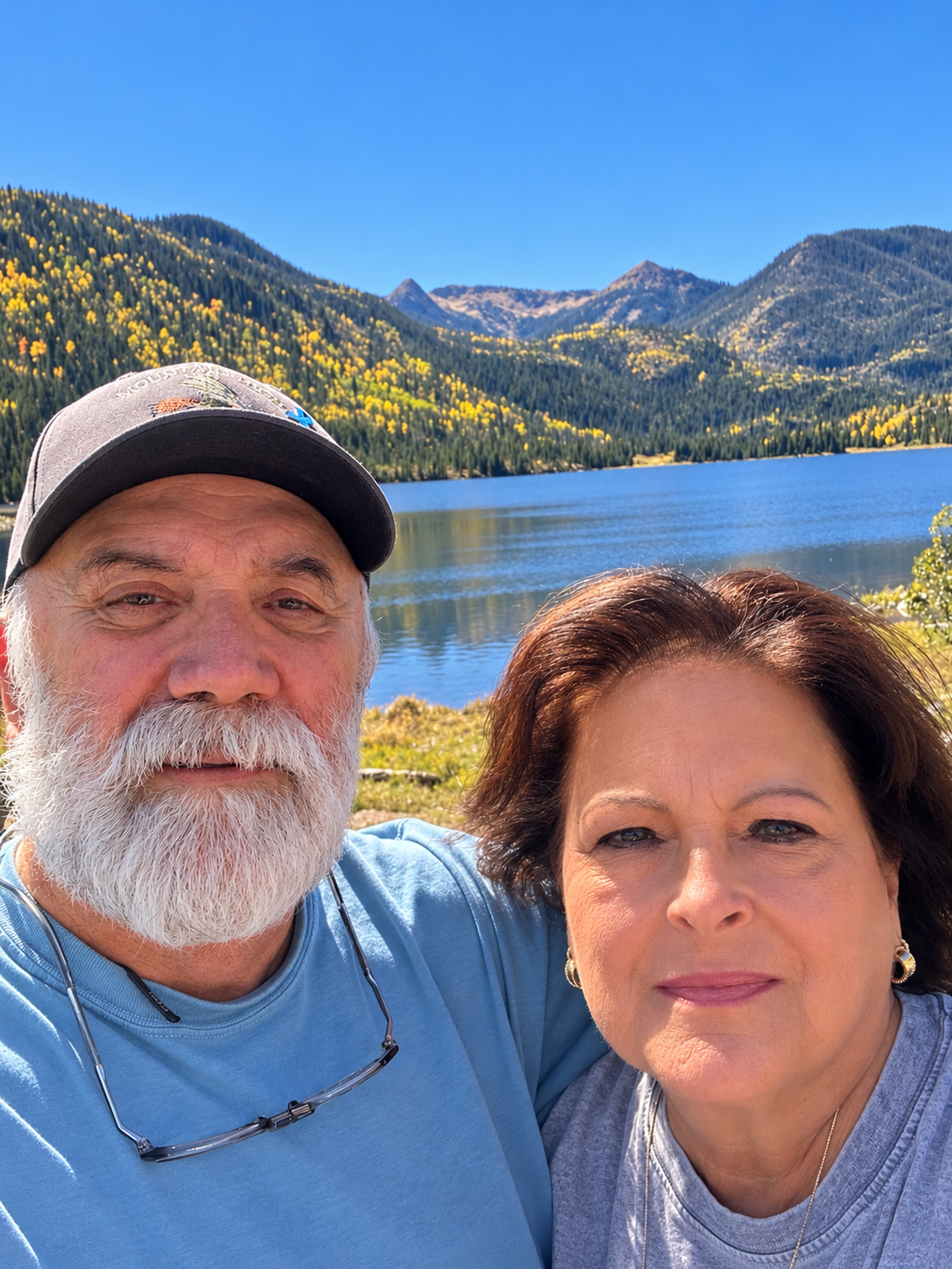 My wife and I taking a selfie beside a Rocky mountain lake surrounded by autumn-colored forests