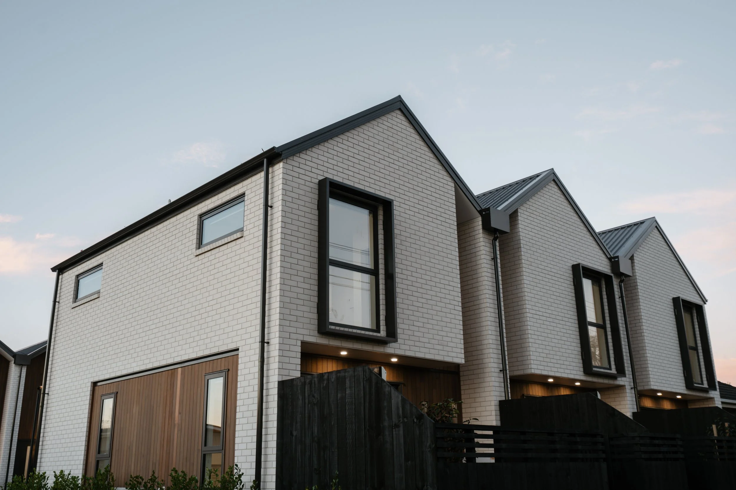 Modern white brick townhouse with large windows, black accents, and a copper roof, taken at dusk.