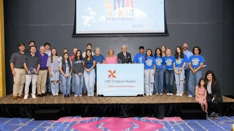 Group of people on stage at UMC Children's Hospital event, with a large screen behind them and a podium displaying the hospital logo.