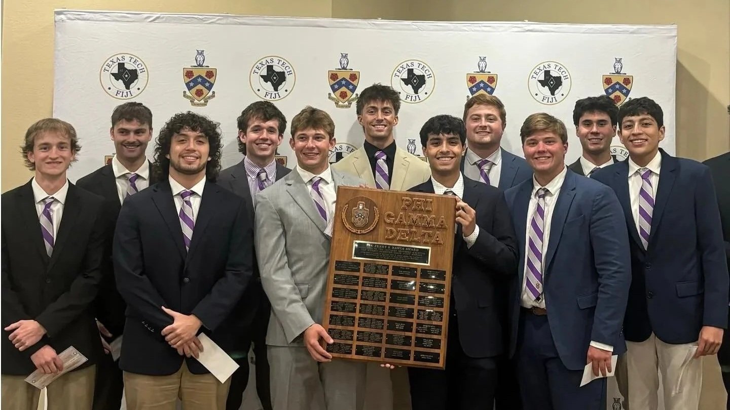 A group of young men in suits holding a wood plaque with the Ohio Alpha Delta Pi crest, standing in front of a backdrop with logos of Texas Tech University.