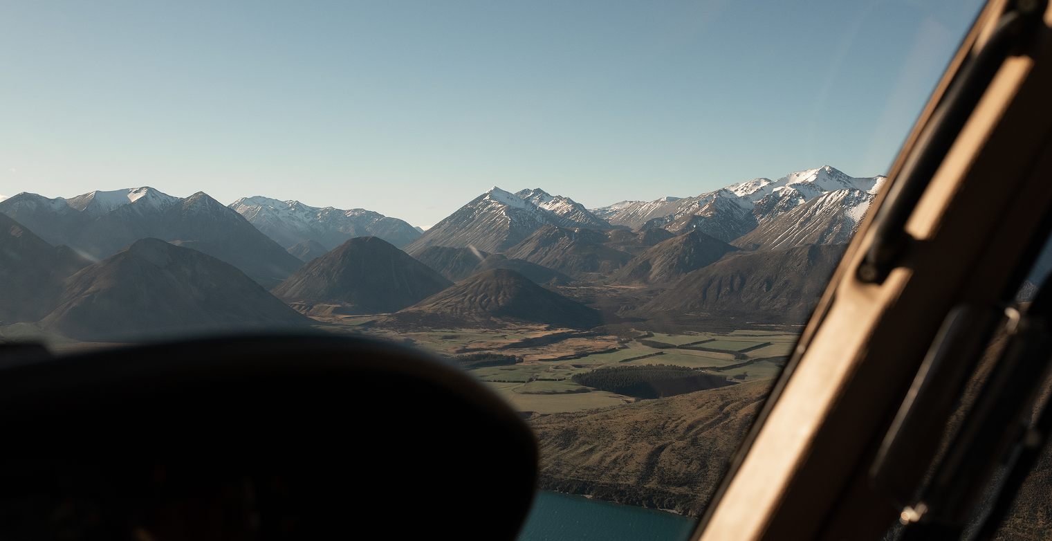 Aerial view of snow-capped mountains over green fields seen through an aircraft window.