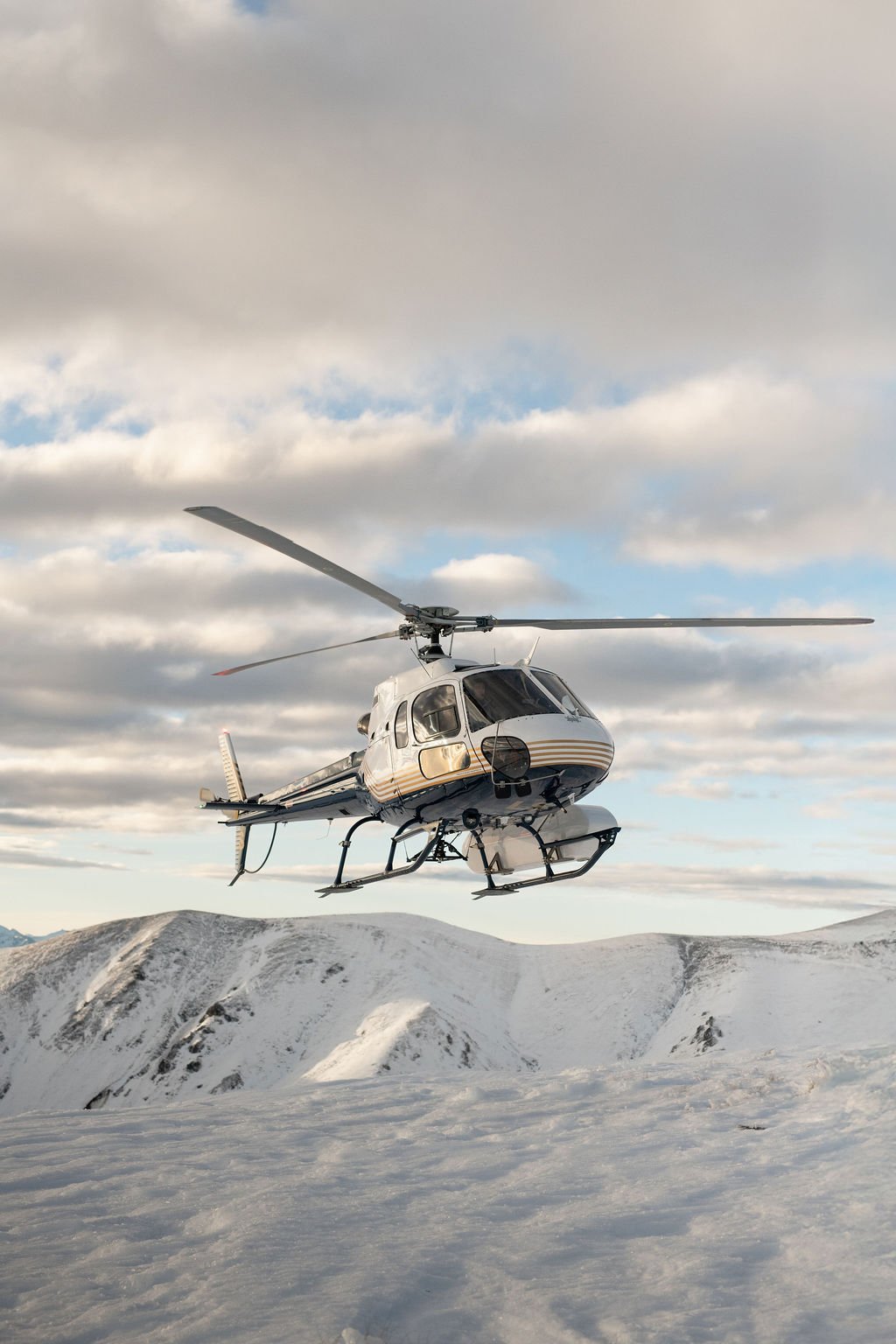 A helicopter flying over snow-covered mountains on a cloudy day.