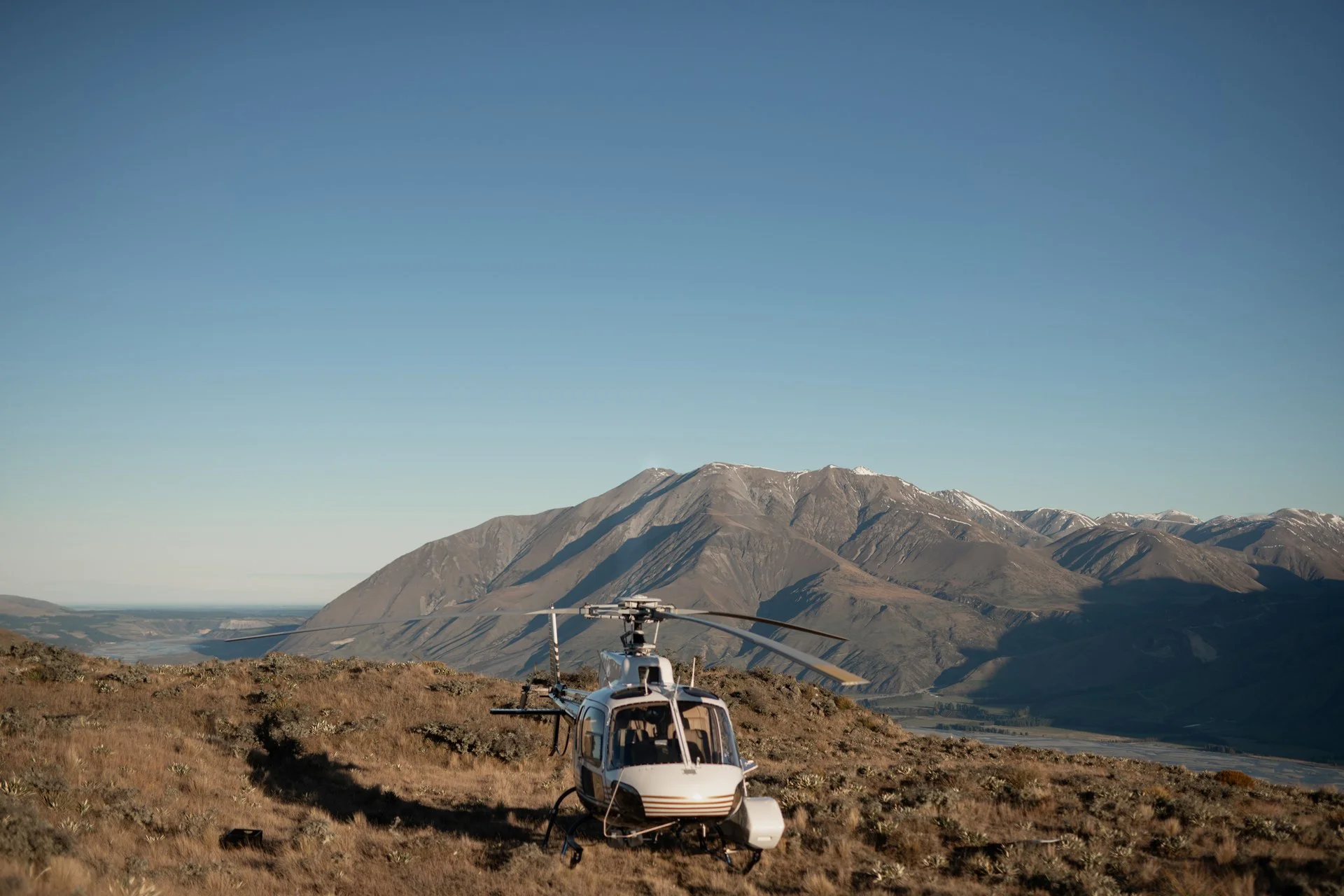 A helicopter on a mountain landscape with mountains and a clear blue sky in the background.