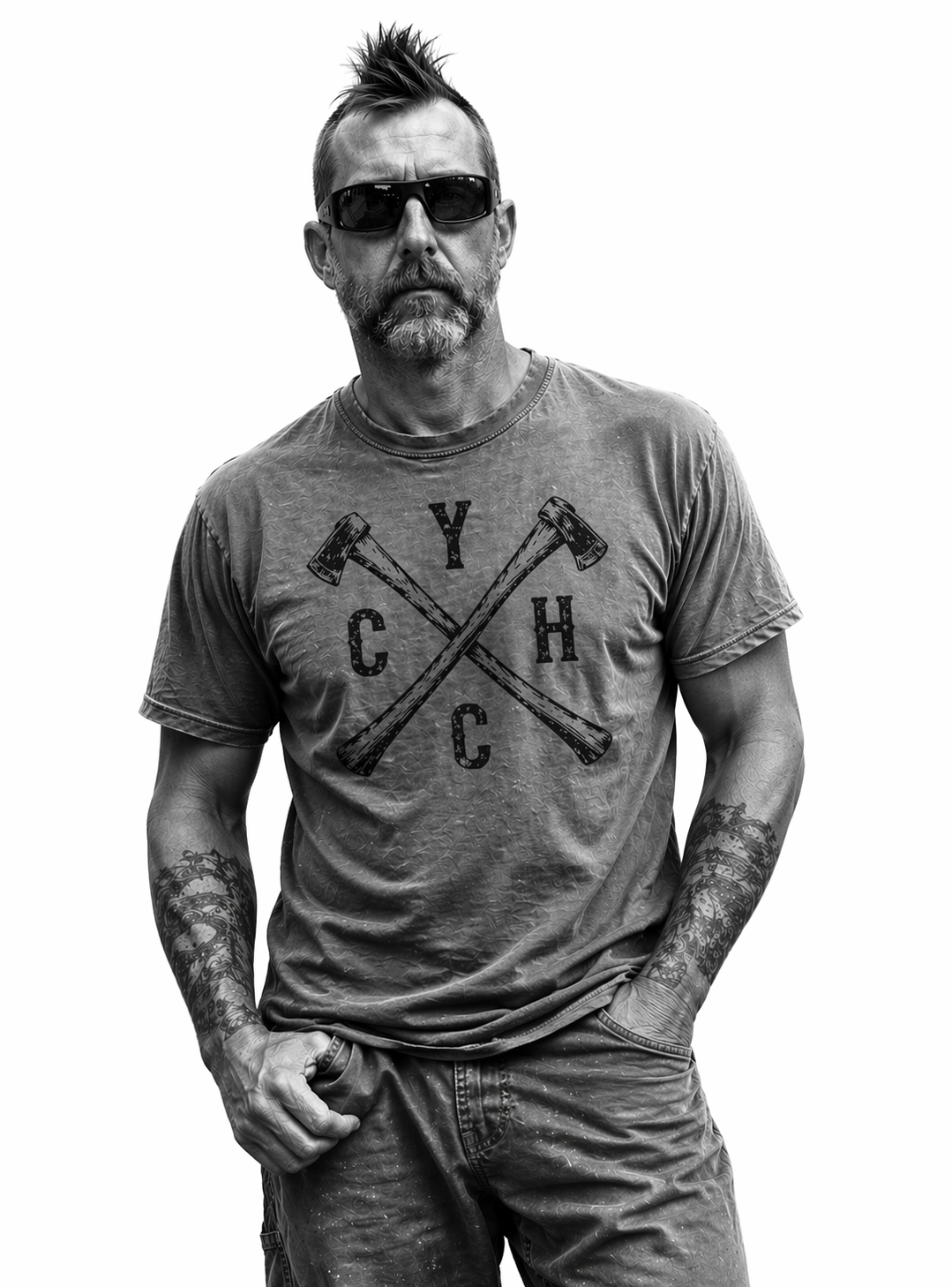 Black and white photo of a man with spiked hair, sunglasses, a beard, tattooed arms, wearing a graphic T-shirt with crossed hammers and the letters Y, C, H, C, and jeans.