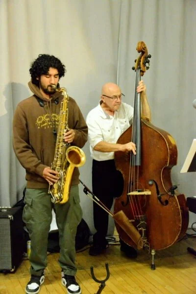 Two jazz musicians performing indoors, one playing a saxophone and the other playing a double bass.