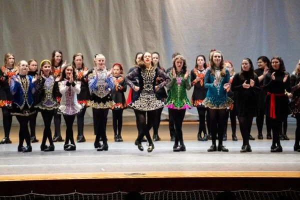 Group of young girls performing a dance on stage, wearing colorful costumes with black tights and shoes.