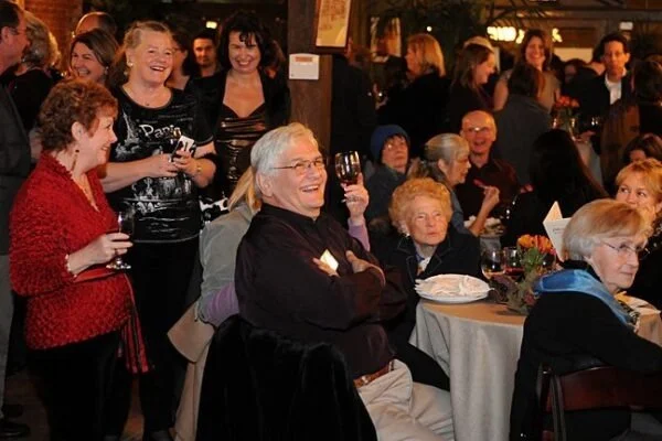 Group of people at a social gathering in a restaurant, smiling and enjoying drinks.