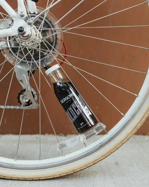 A bicycle wheel with a tube of dietary supplement labeled 'Seasonal MCT' attached to the spokes near the hub.