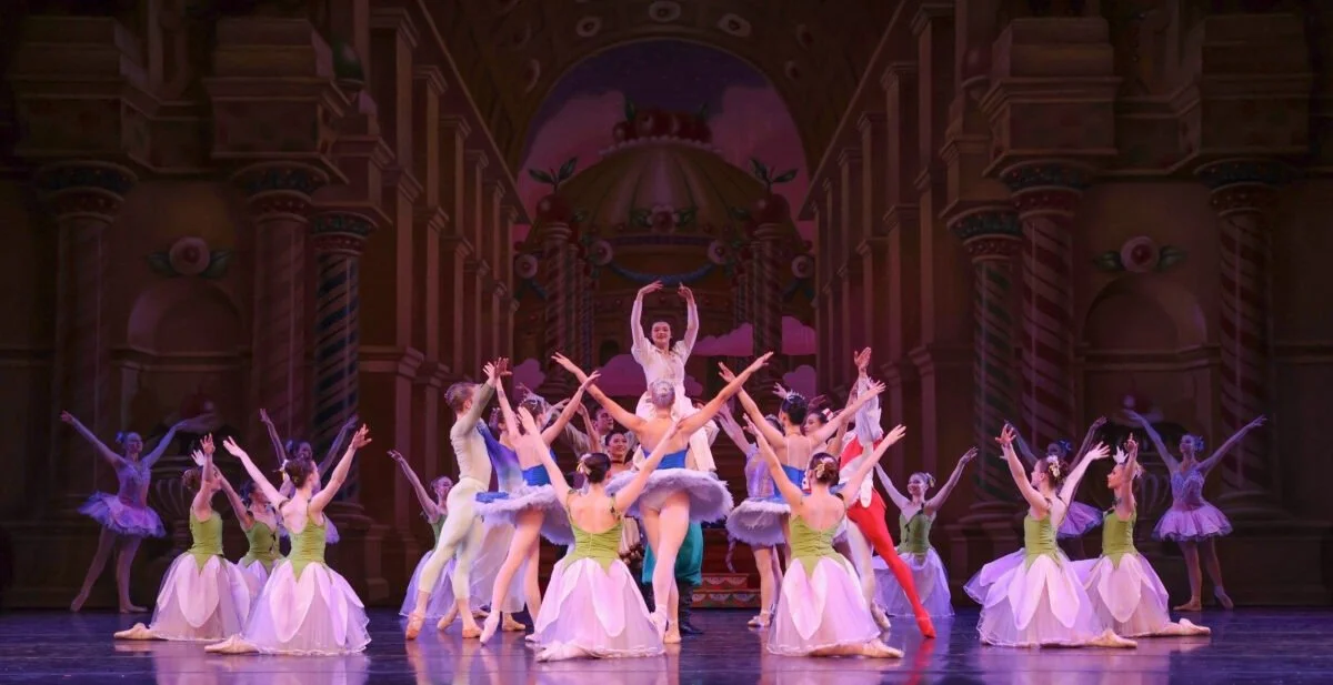 Ballet dancers on stage performing a classical ballet in a theater with ornate architecture.